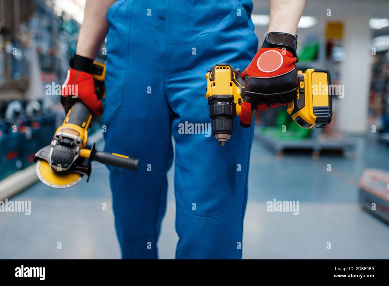 Un travailleur mâle tient un tournevis à batterie et une meuleuse d'angle dans le magasin d'outils. Choix d'équipements professionnels dans l'atelier de quincaillerie, instruments électriques Banque D'Images