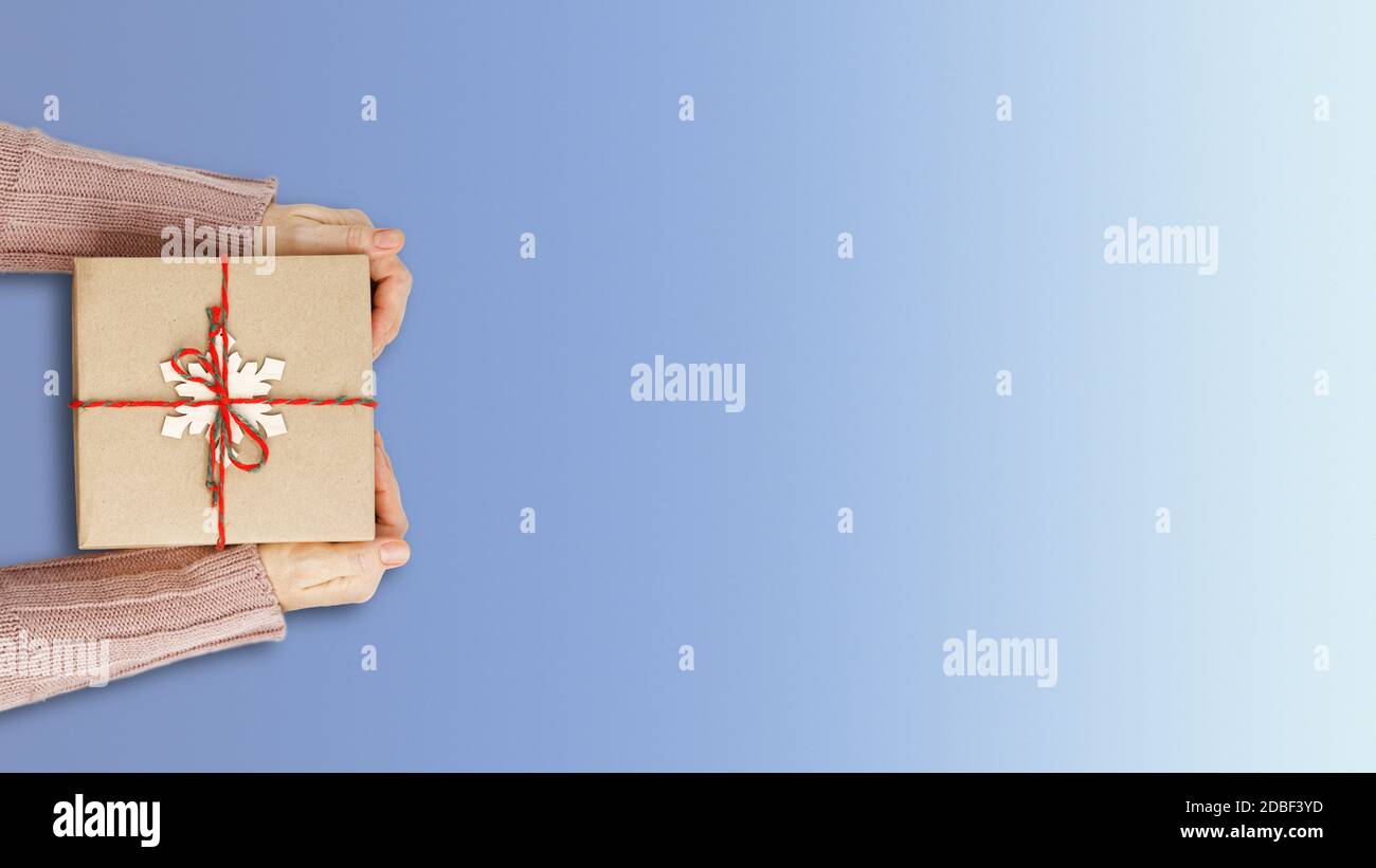Les mains des femmes tenant une boîte cadeau enveloppée dans du papier kraft et attachée avec de la ficelle sur fond bleu gadient. Vue de dessus. CopySpace. Banque D'Images Les mains des femmes tenant une boîte cadeau enveloppée dans du papier kraft et attachée avec de la ficelle sur fond bleu gadient. Vue de dessus. CopySpace. Banque D'Images