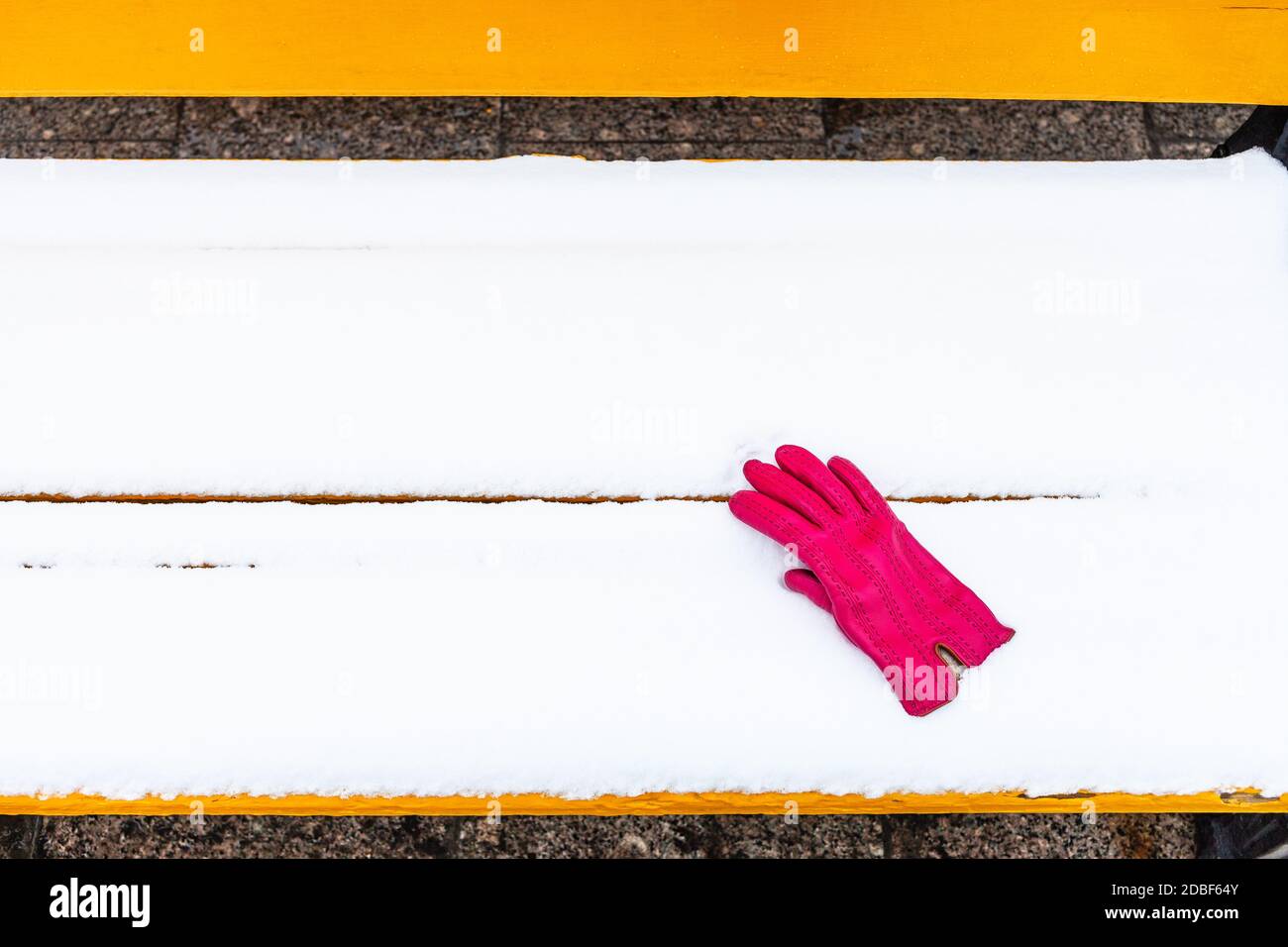 gant rouge oublié de femme sur banc en bois jaune recouvert de neige en hiver Banque D'Images