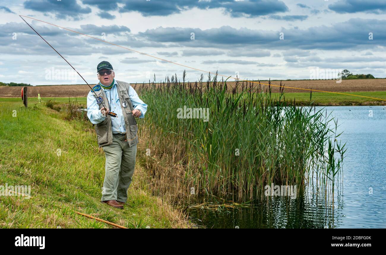Lincolnshire, Royaume-Uni - M. Barry Grantham, un instructeur de pêche à la mouche, jetant une ligne de mouche à travers un lac de truite pour la truite arc-en-ciel Banque D'Images Lincolnshire, Royaume-Uni - M. Barry Grantham, un instructeur de pêche à la mouche, jetant une ligne de mouche à travers un lac de truite pour la truite arc-en-ciel Banque D'Images