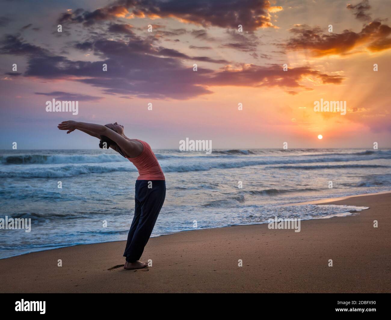 Jeune femme sportive faisant du yoga Sun salutation Surya Namaskar Posez Hasta Uttanasana sur la plage tropicale au coucher du soleil Banque D'Images