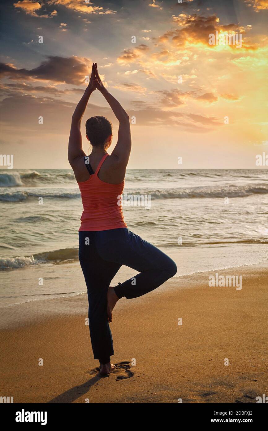Yoga à l'extérieur - femme sportive faisant Hatha yoga asana Vrikshasana tre pose sur la plage tropicale au coucher du soleil Banque D'Images