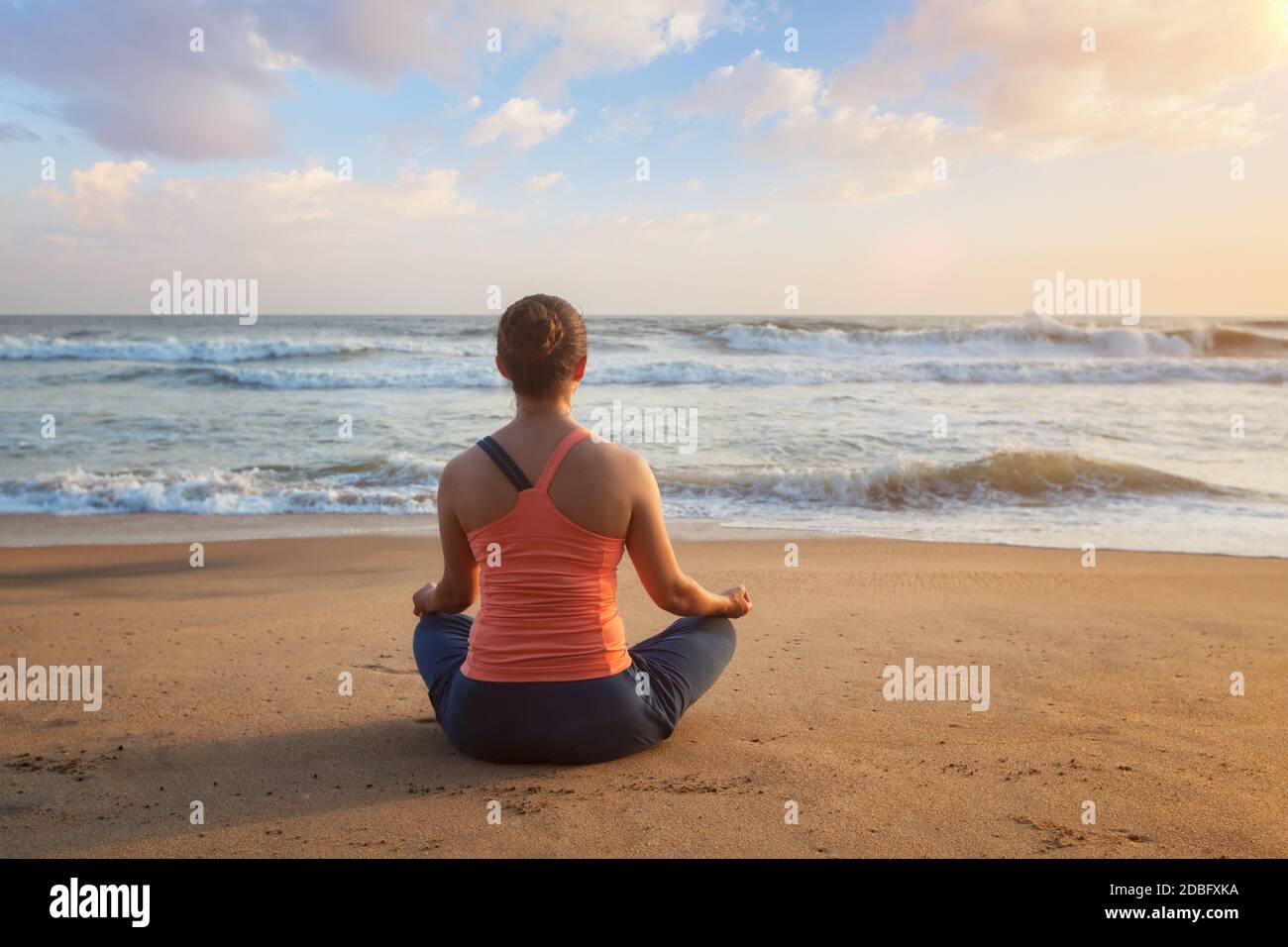 Femme faisant du yoga - méditer et se détendre dans Padmasana Lotus Posez à l'extérieur sur la plage tropicale au coucher du soleil Banque D'Images