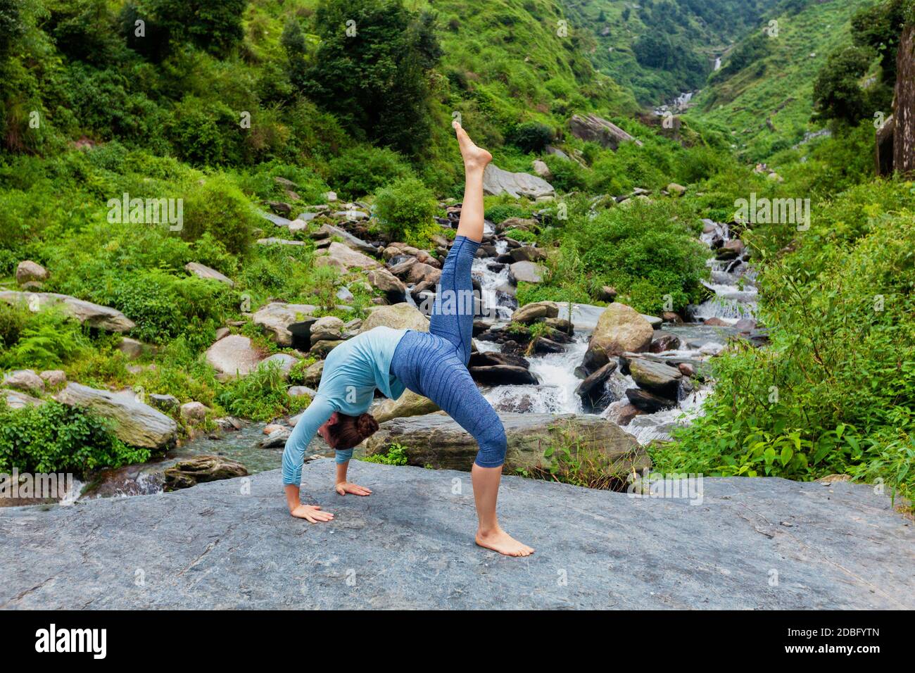 Outdoors de yoga - femme faisant du yoga asana eka pada urdva Dhanurasana vers le haut Bow poser arrière benkd à l'extérieur à la chute d'eau dedans Himalaya Banque D'Images