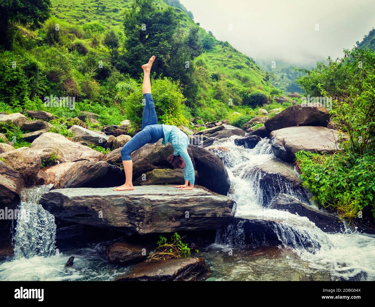 Outdoors de yoga - femme faisant du yoga asana eka pada urdva dhanurasana remonter Bow poser dos benkd dehors à la cascade dans l'Himalaya. Effet rétro vintage Banque D'Images