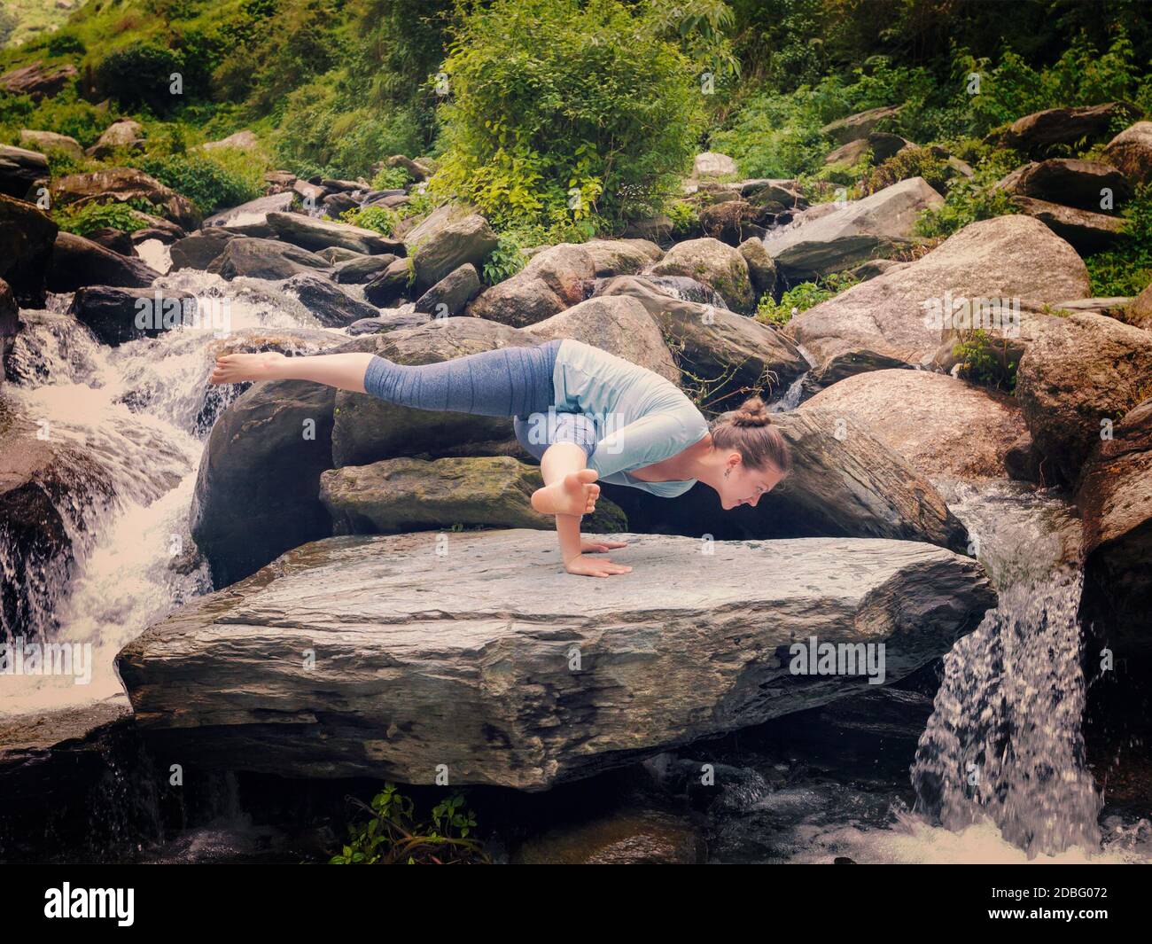 Jeune femme sportive faisant du yoga asana Eka Pada Koundinyasana 1 à la cascade tropicale. Image style boxer style rétro avec filtre. Banque D'Images