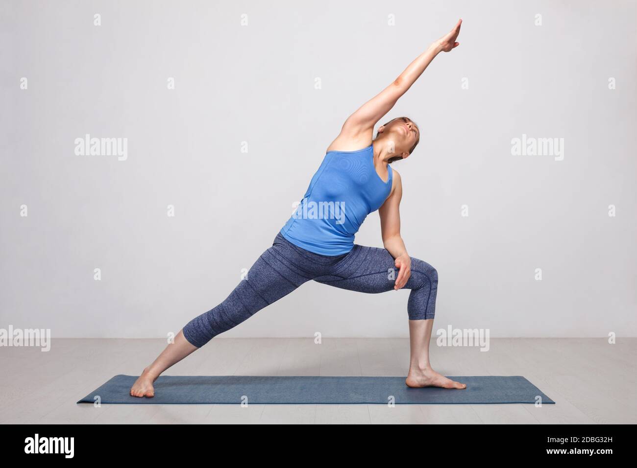 Femme faisant Ashtanga Vinyasa yoga asana Utthita parsvakonasana - étendu angle latéral poser la variation débutant sur le tapis de yoga sur le yoga tapis en studio sur gris Banque D'Images