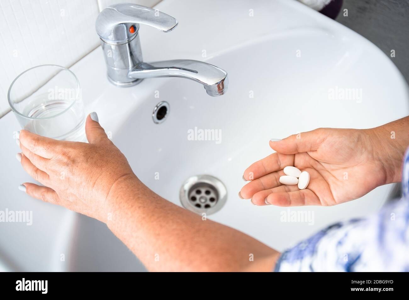 La femme âgée boit des pilules ou des vitamines, la dose quotidienne de médicaments. Gros plan les mains des femmes âgées avec des pilules et un verre d'eau à la maison. Médecine Banque D'Images