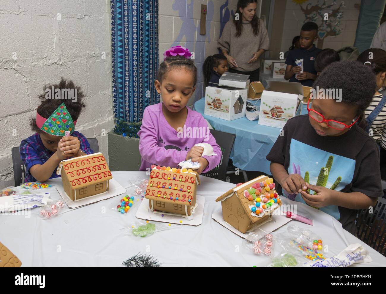 Les enfants privilégiés construisent et décorent des maisons en pain d'épice lors d'une fête de Noël dans un centre communautaire de Manhattan, New York. Banque D'Images