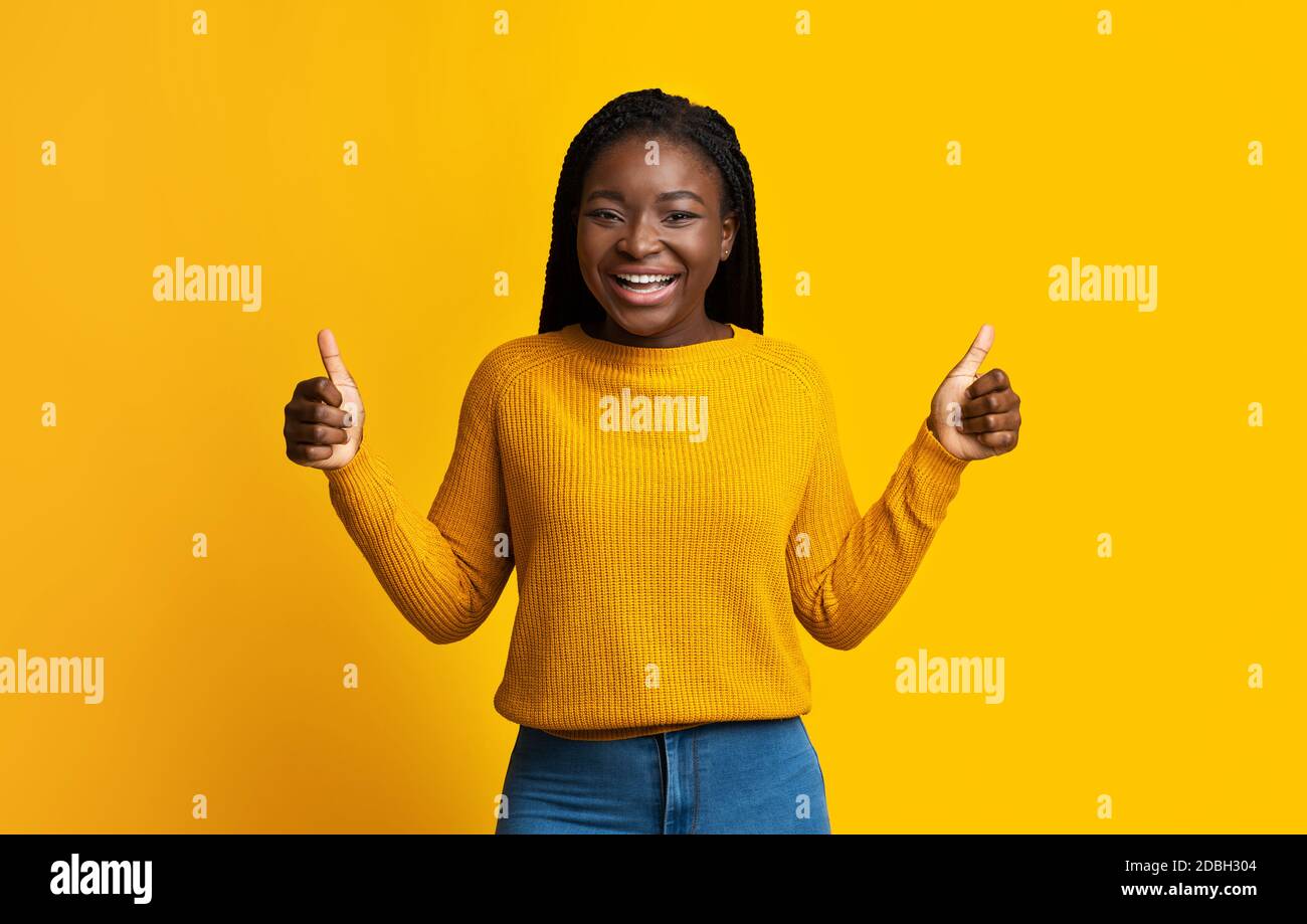 J'aime ça. Joyeuse femme africaine en chandail brillant montrant des Thumbs Up Banque D'Images