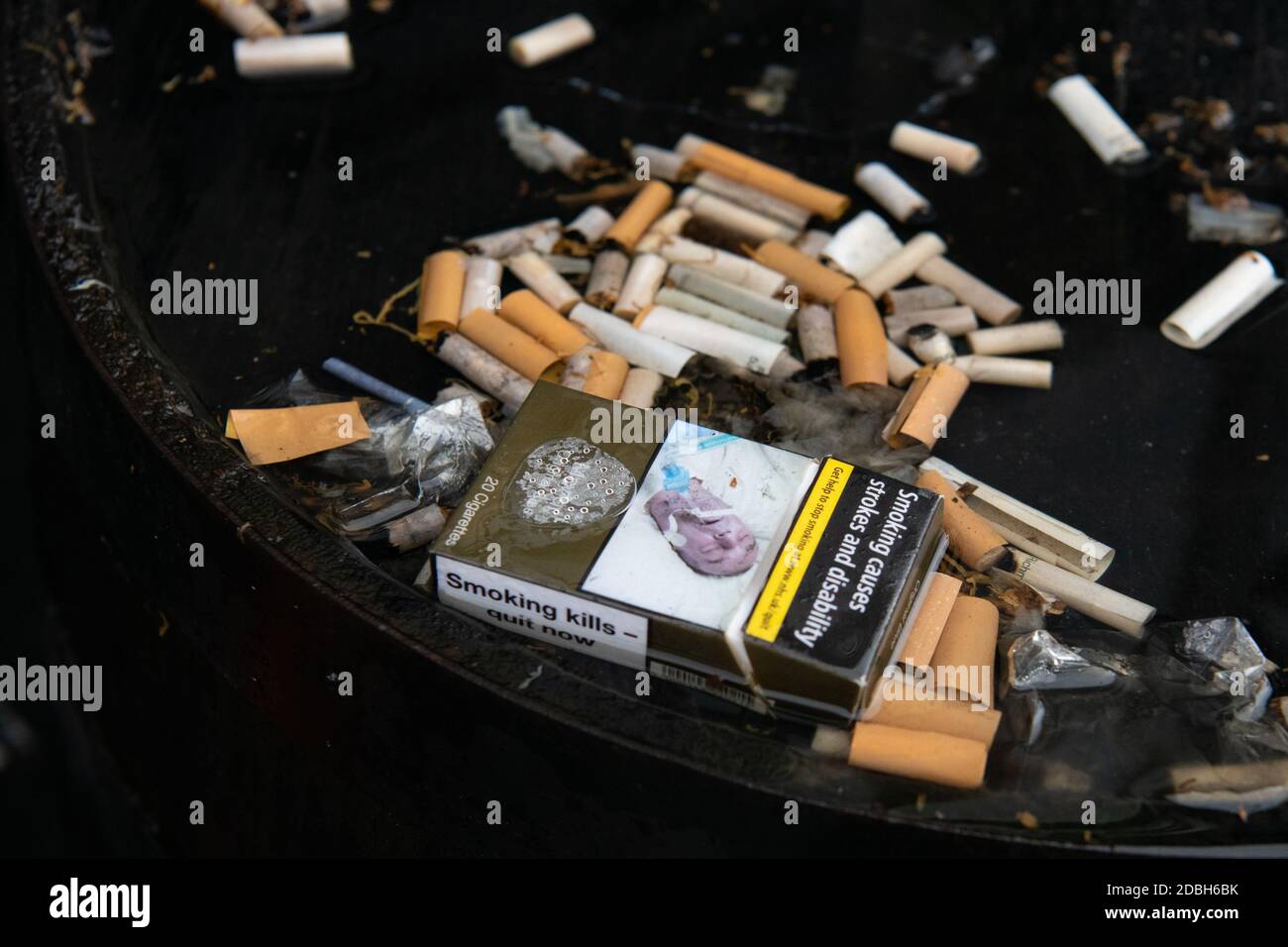 Cigarettes - mégots de cigarettes et paquet vide avec des avertissements sanitaires - dans l'eau de pluie sur le dessus du baril de whisky à l'extérieur du pub - Écosse, Royaume-Uni Banque D'Images