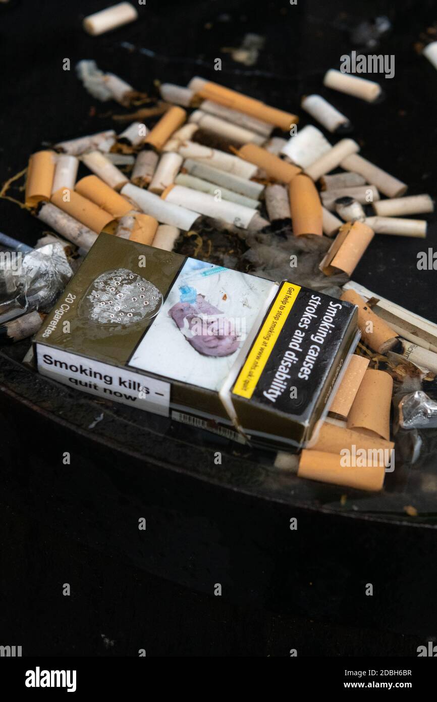 Cigarettes - mégots de cigarettes et paquet vide avec des avertissements sanitaires - dans l'eau de pluie sur le dessus du baril de whisky à l'extérieur du pub - Écosse, Royaume-Uni Banque D'Images