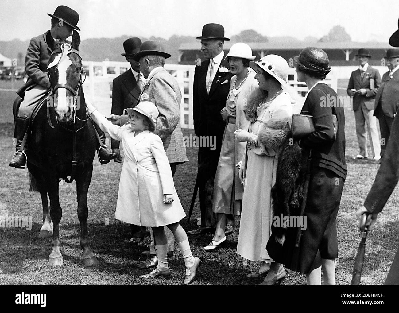 Elizabeth II petant un cheval au Royal Horse Show à Richmond, Surrey. De gauche à droite : le roi George V. (légèrement caché), le duc d'Athlone et sa femme, la marquise de Cambridge et la reine Elizabeth. Banque D'Images