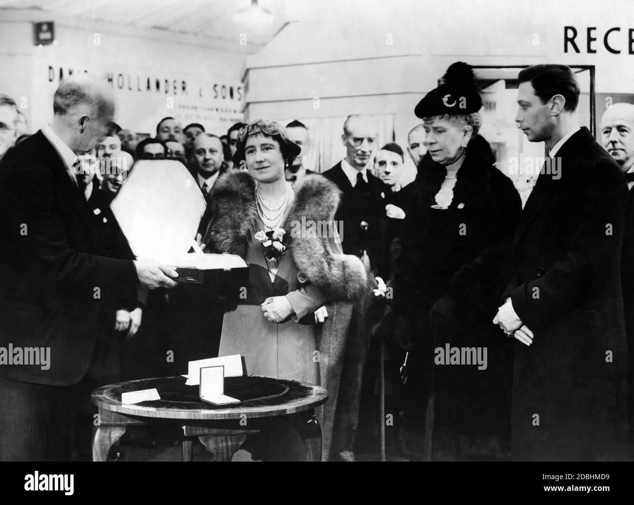 La reine Elizabeth, la reine mère Mary et le roi George VI au British Industries Fair à Olympia, Londres, pour marquer le jubilé d'or de la fondation de l'association des joyaux et des silversmith de Birmingham. La Reine reçoit un émail doré argenté et un ensemble de toilettes opale. Elle porte un manteau bleu avec la fourrure de renard argenté et la reine Mary un manteau de velours noir avec la fourrure de renard argenté. Banque D'Images