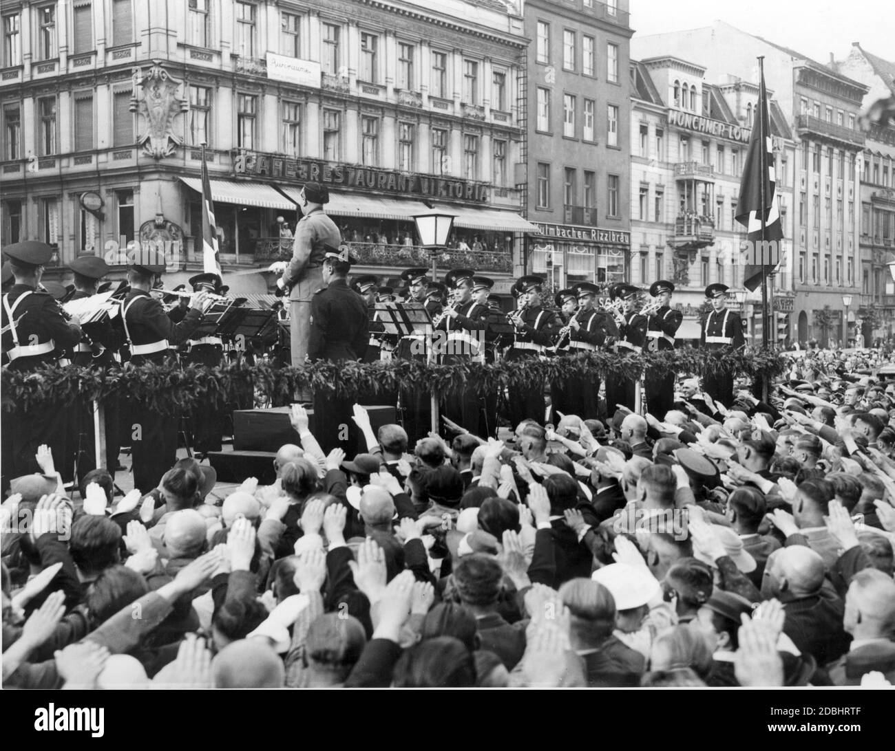 L'Academia Musica de l'Opéra Nazionale Balilla (organisation de jeunesse des fascistes italiens) joue un concert au Kranzler-Ecke (boulevard Unter den Linden, angle Friedrichstrasse) à Berlin en 1937. La foule interprète le salut nazi. Certaines personnes écoutent également la terrasse du café et restaurant Viktoria. À côté de l'hôtel se trouvent le Kulmbacher Rizzibraeu et le Munich Loewenbraeu. Banque D'Images