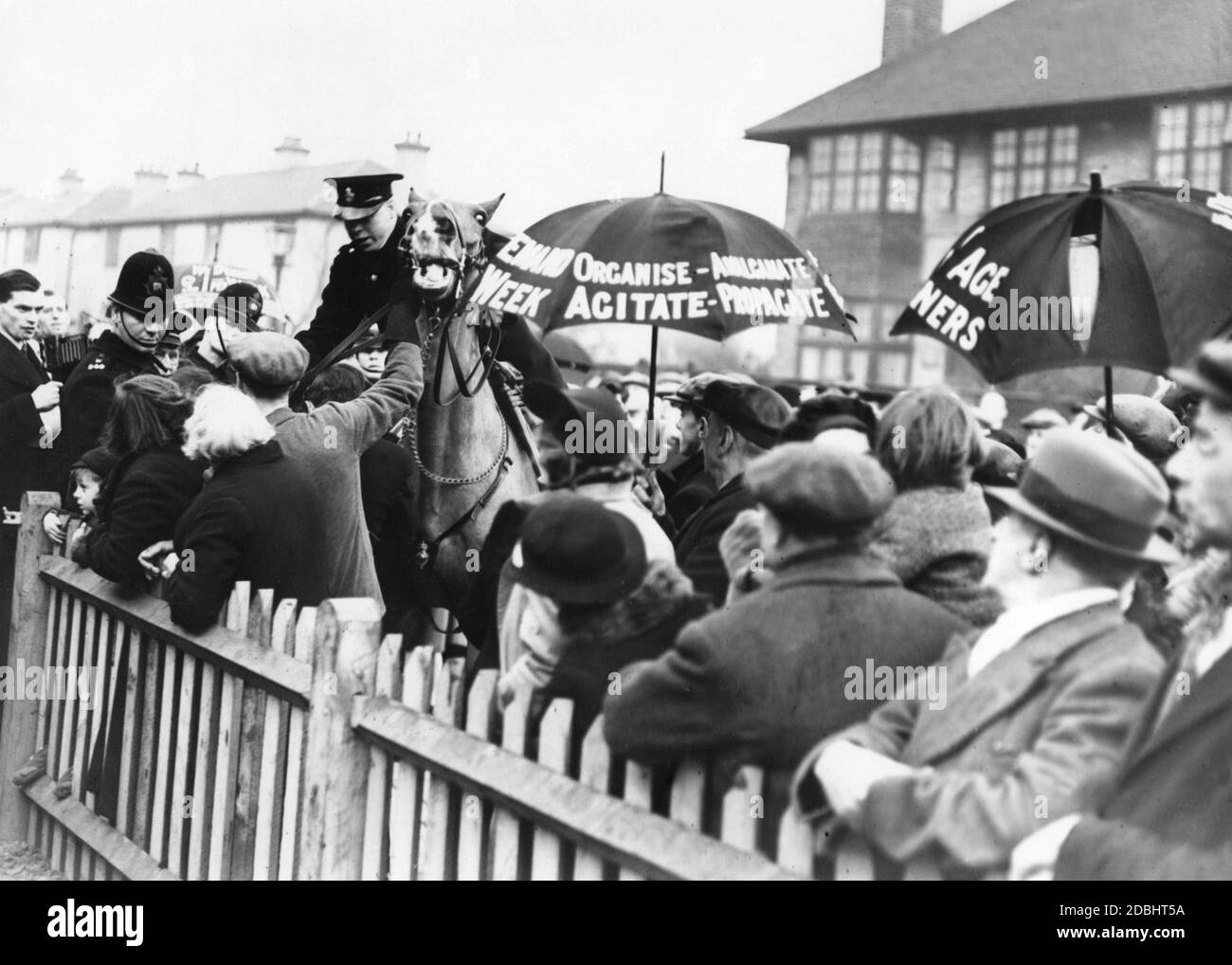Des policiers montés tentent de disperser une manifestation dans la rue Denmark, dans l'est de Londres. Les gens manifestent contre Lady Astor, députée de Sutton, qui a comparu à East End pour l'ouverture de nouvelles maisons de l'Armée de l'Église. D'autres manifestants (avec des parapluies) démontrent également une augmentation des pensions. Banque D'Images