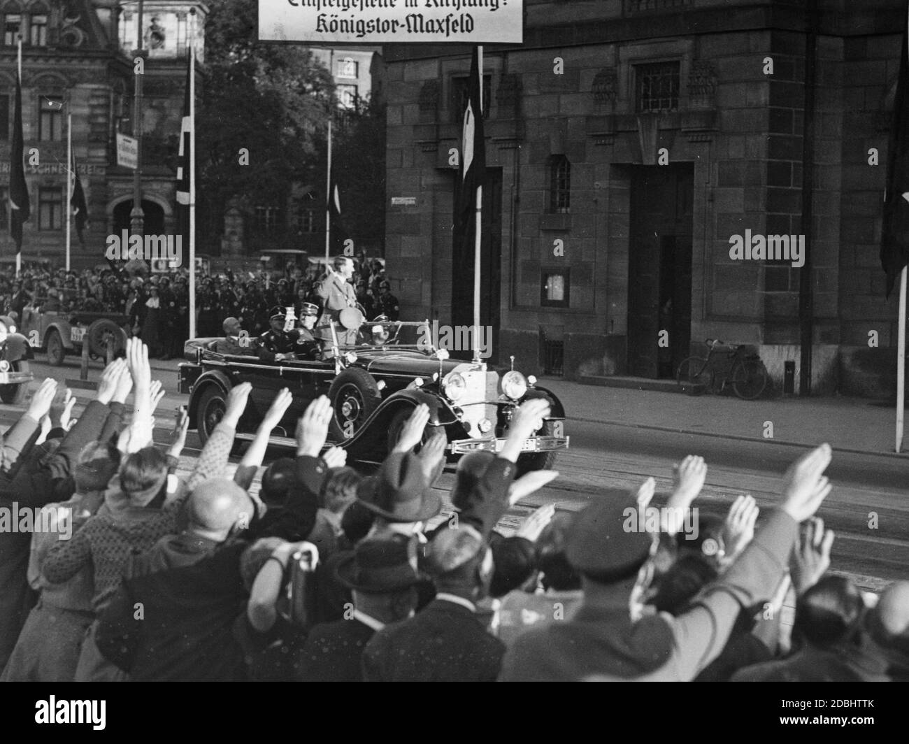 « Adolf Hitler, en Mercedes, avec Julius Schaub assis derrière lui, est accueilli par les gens enthousiastes de Nuremberg et conduit à l'hôtel Deutscher Hof, où il sera resté pendant le Congrès du Parti nazi à Nuremberg. Ci-dessus se trouve un panneau avec l'inscription ''point d'embarquement en direction: Koenigstor-Maxfeld''.' Banque D'Images