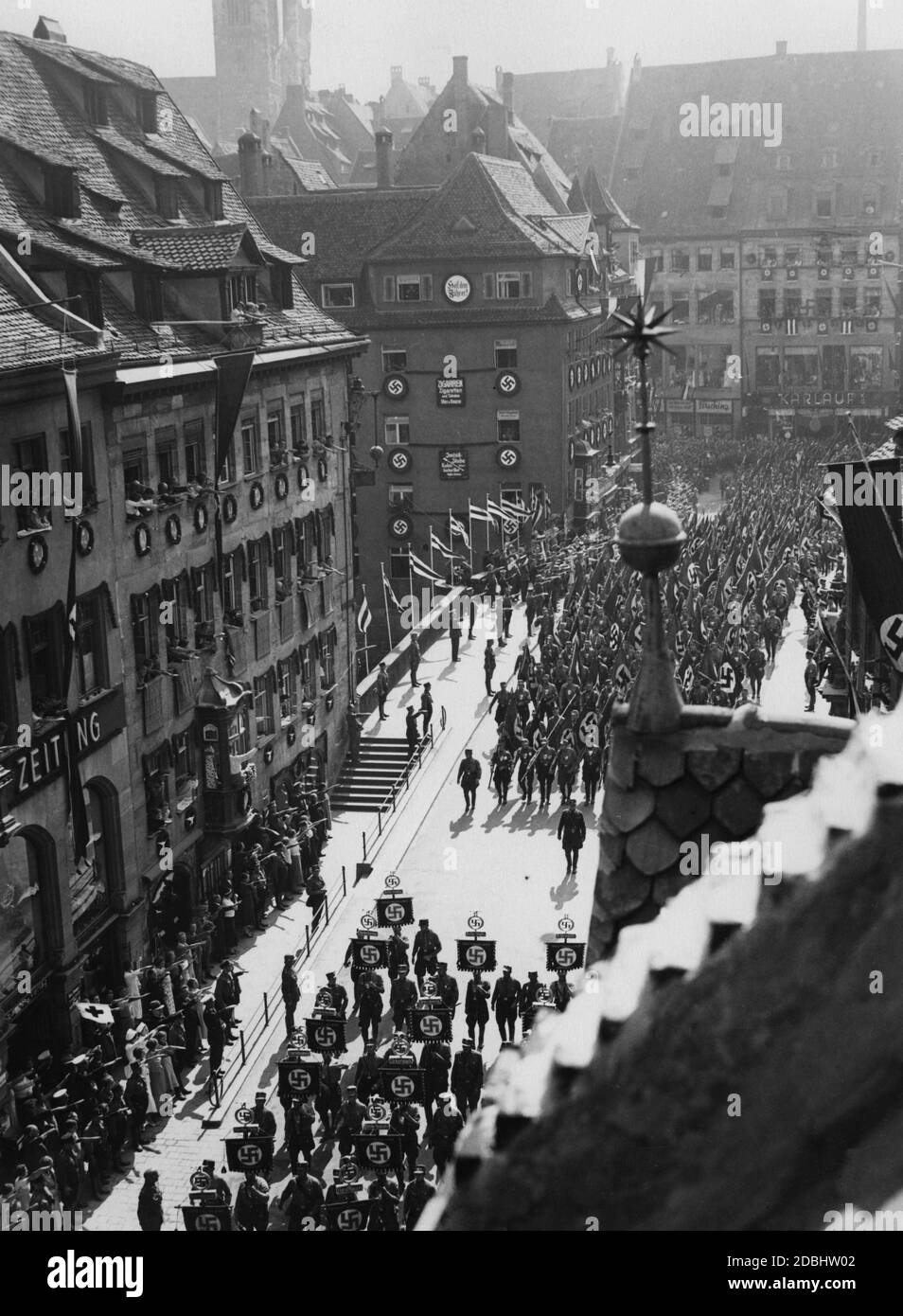 « LES unités DE LA SA traversent le pont Fleisch sur le chemin de la place Adolf-Hitler-Platz. Sur le bâtiment de l'autre côté du pont, sur la gauche, il y a plusieurs swastikas et un panneau indiquant ''Heil dem Fuehrer!'' (''Hail to the Fuehrer''). En bas à gauche, au milieu des spectateurs, il y a plusieurs infirmières. Banque D'Images
