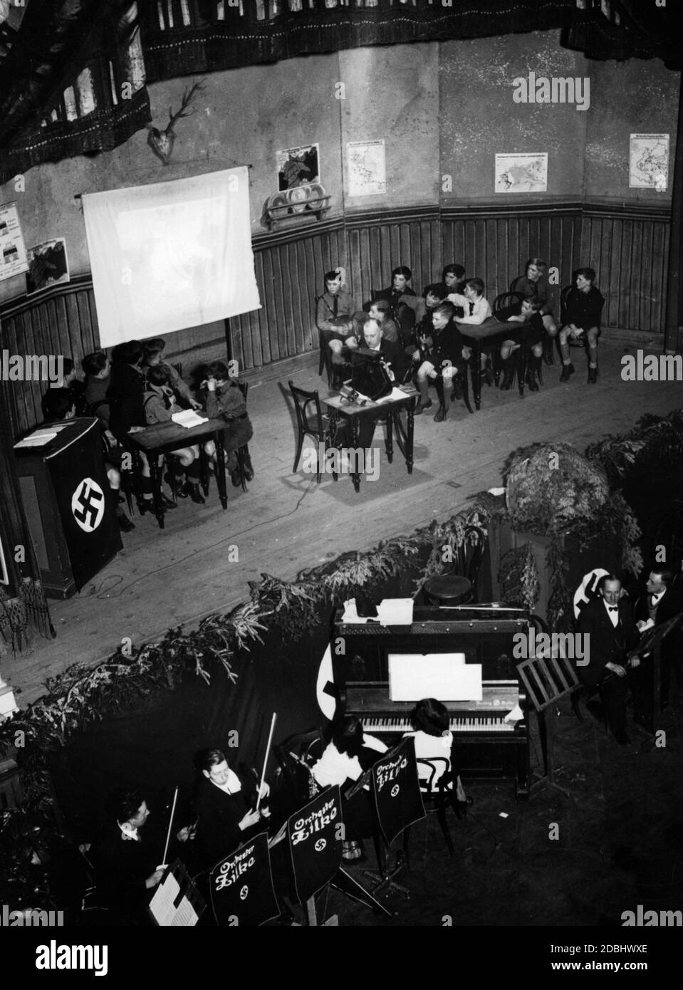 'Les élèves d'une école élémentaire de Berlin présentent sur scène leur jeu de propagande ''Jochen hilft im Luftschutz'', avec le chant de l'Horst-Wessel-Lied accompagné de l'orchestre d'école Zilko. A gauche, il y a un podium des enseignants avec un drapeau swastika." Banque D'Images