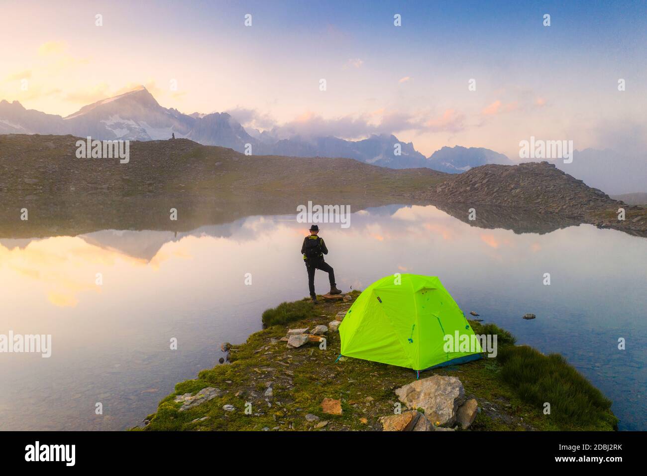 Vue arrière de l'homme avec chapeau debout à l'extérieur de la tente au lac Obere Schwarziseeli à l'aube, col de Furka, canton d'Uri, Suisse, Europe Banque D'Images