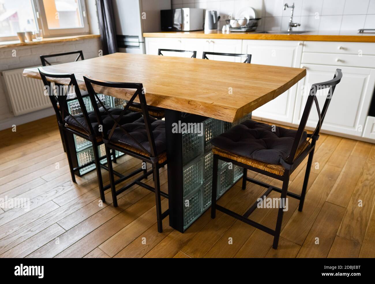 Une grande table à manger en bois avec des blocs de verre et des chaises et  oreillers en osier en métal dans la scandinave moderne une cuisine à manger,  contre le sol