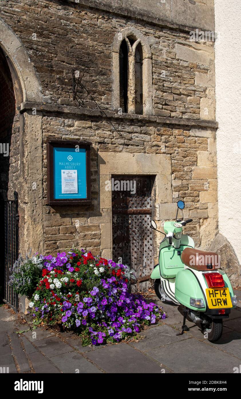 Malmesbury, Wiltshire, Angleterre, Royaume-Uni. 2020. Un scooter et une exposition de fleurs à la porte d'entrée de l'abbaye de Mmalesbury datant du 12ème siècle Banque D'Images