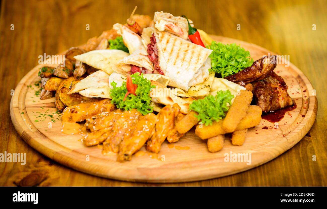 Calories élevé pour le groupe d'amis. De délicieux en-cas savoureux. Les repas au restaurant. Snack pour la bière. Planche de bois avec beaucoup de frites et bâtonnets de poisson viande burrito steak servi avec une salade. Menu snack-bar. Banque D'Images