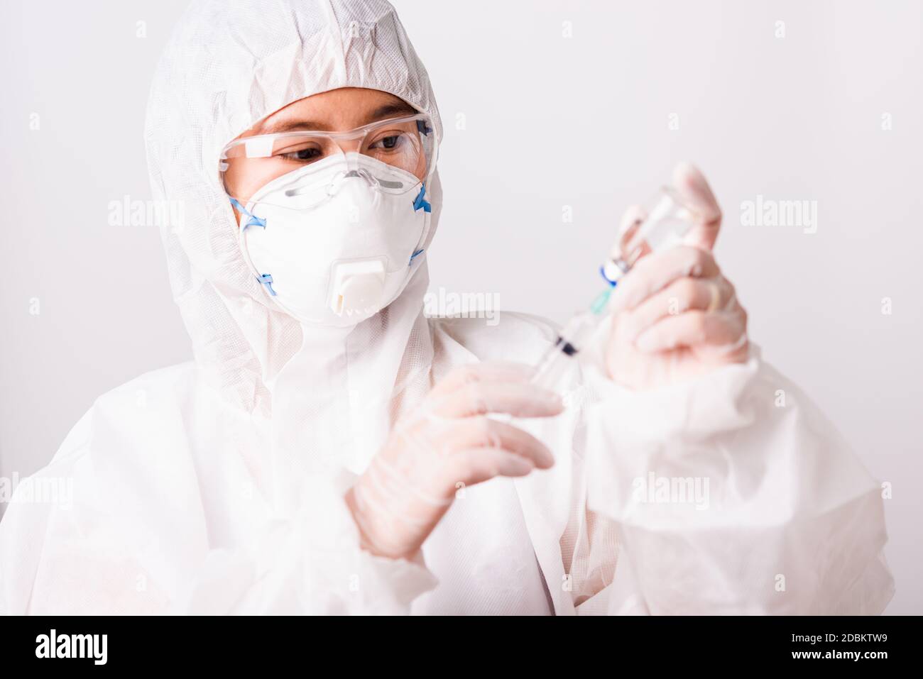 Gros plan de la main de médecin ou scientifique de femme dans la suite EPI uniforme porter masque de protection en laboratoire tenir médicament liquide vaccin flacon et syring Banque D'Images