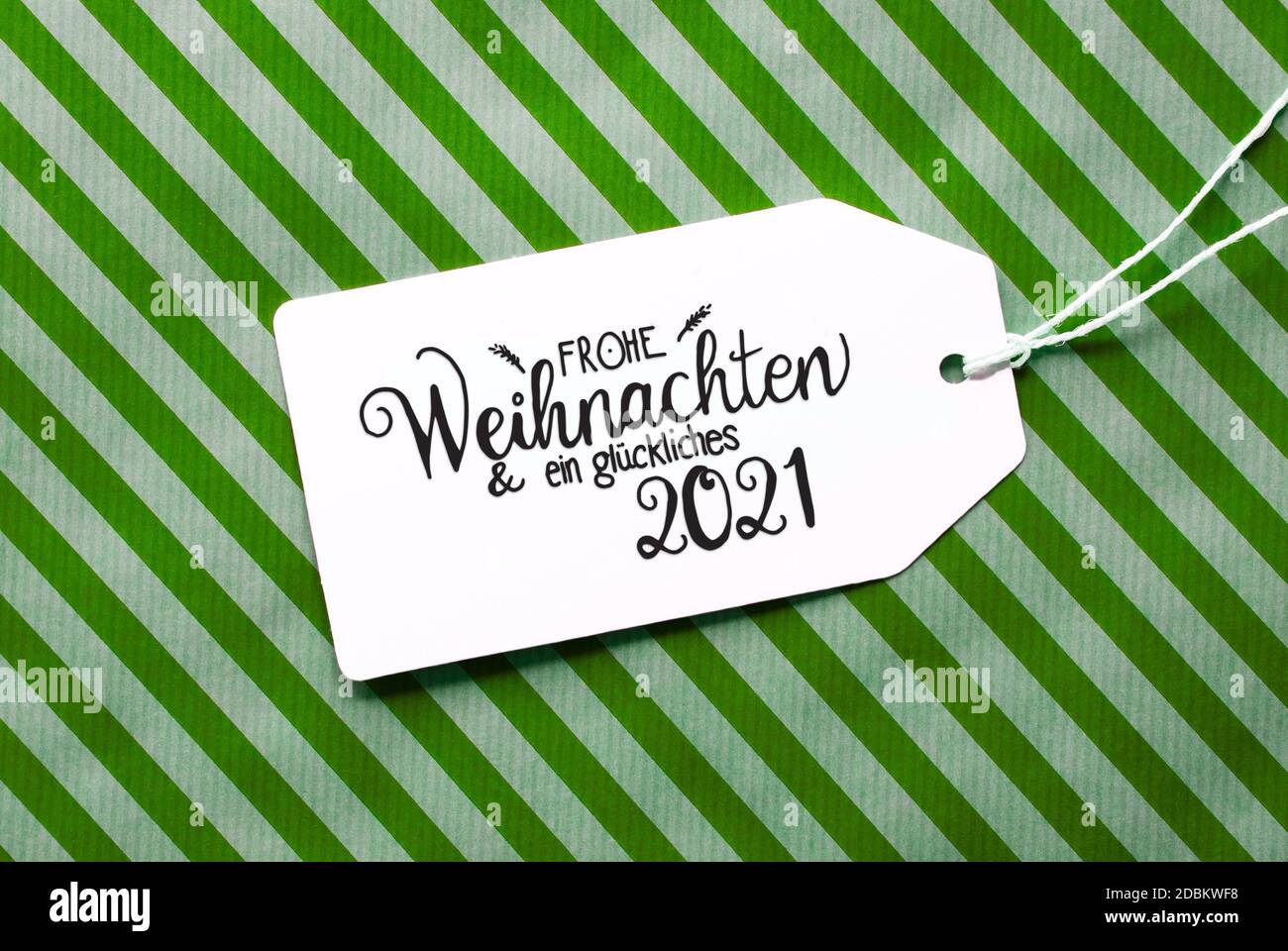 Label avec la calligraphie allemande Frohe Weihnachten und Ein Glueckliches 2021 signifie Joyeux Noël et UN heureux 2021. Papier d'emballage vert comme arrière-plan Banque D'Images