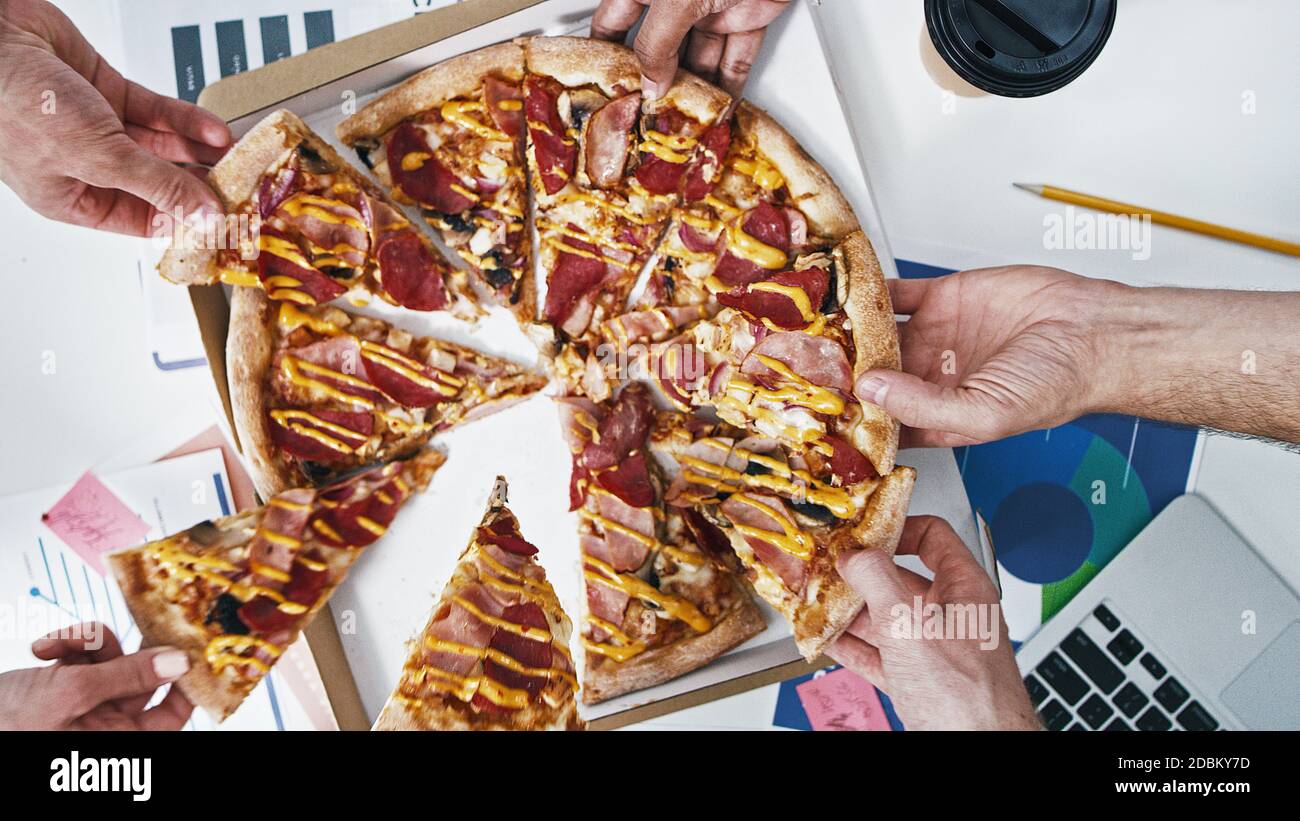 Les gens prennent une pizza au déjeuner dans le bureau de la création. Différentes mains prenant Pizza. Manger au travail. Restauration rapide Banque D'Images