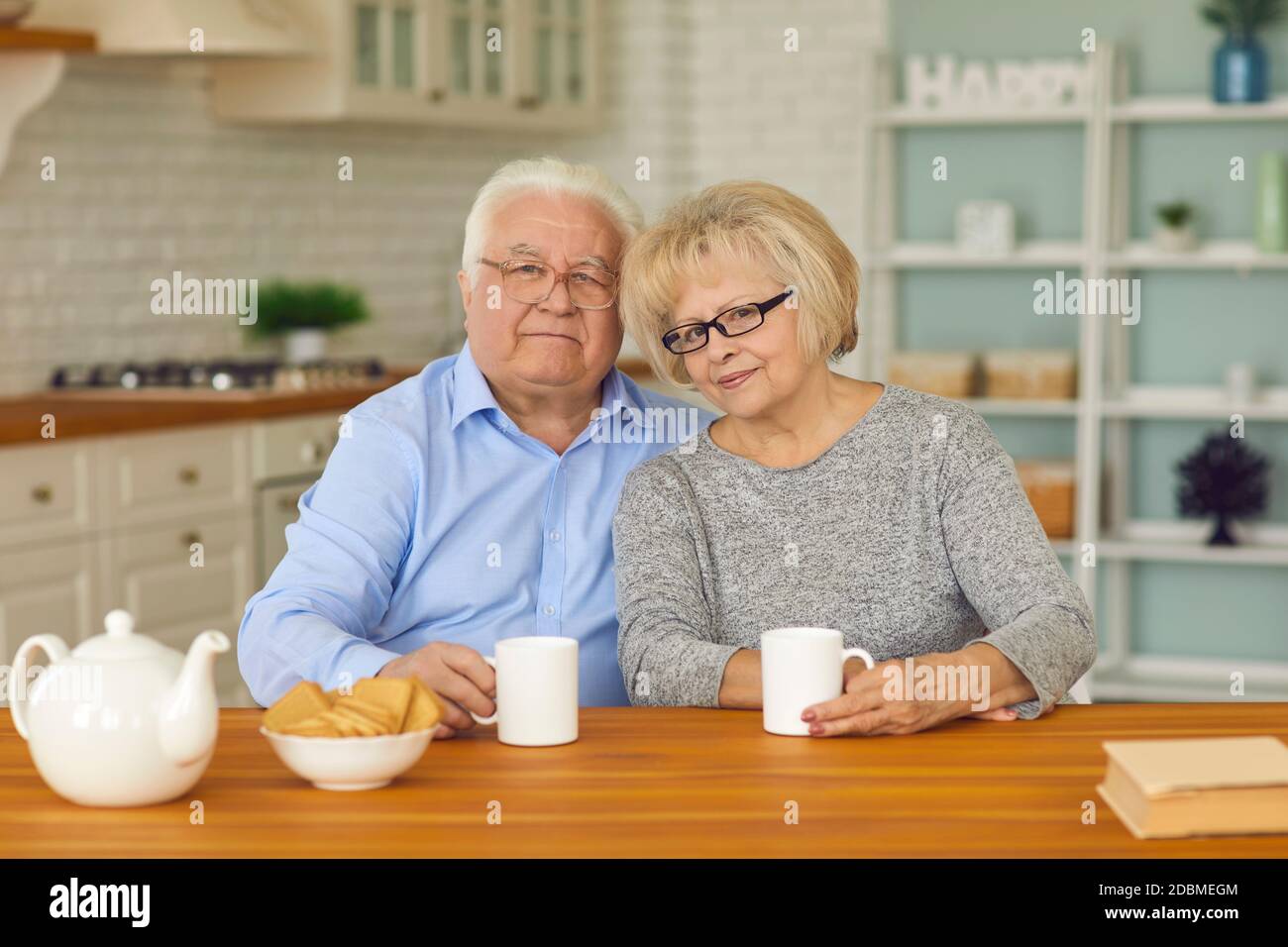 Couples retraités souriants grands-parents assis ensemble dans la cuisine avec thé et biscuits Banque D'Images