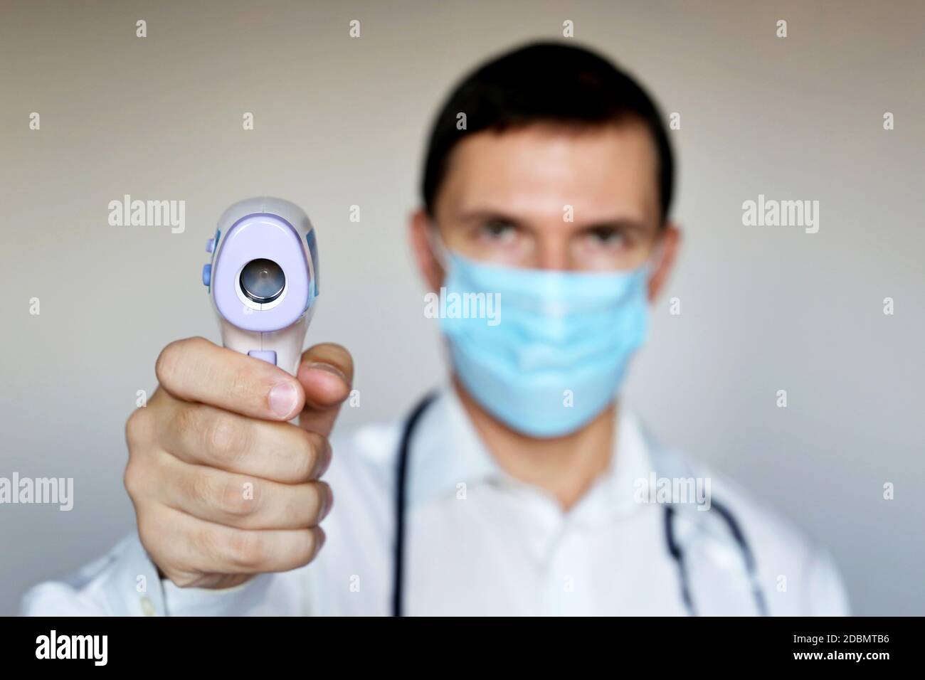 L'homme en masque médical mesure la température corporelle, les symptômes du coronavirus. Médecin avec thermomètre numérique isométrique sans contact dans sa main Banque D'Images