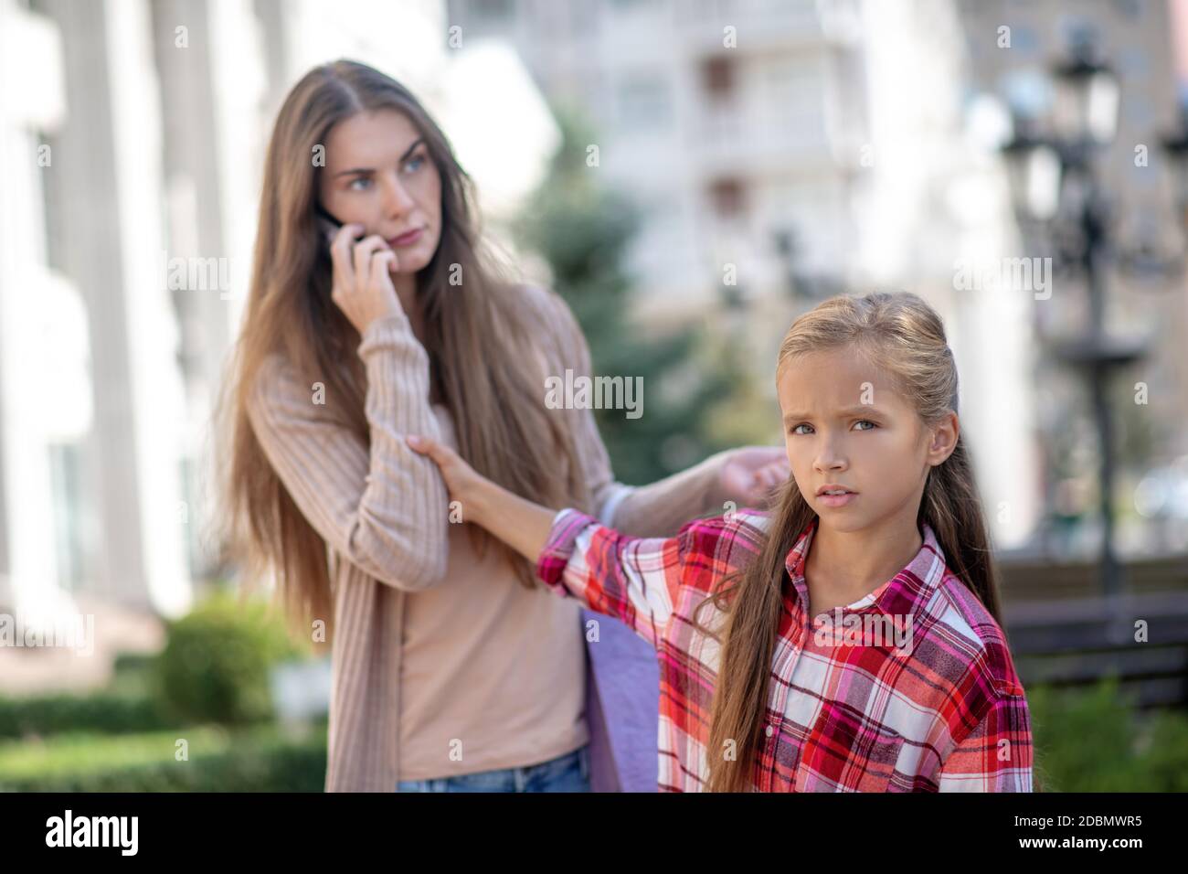 Triste fille tirant la main de sa mère, parlant sur son téléphone Banque D'Images