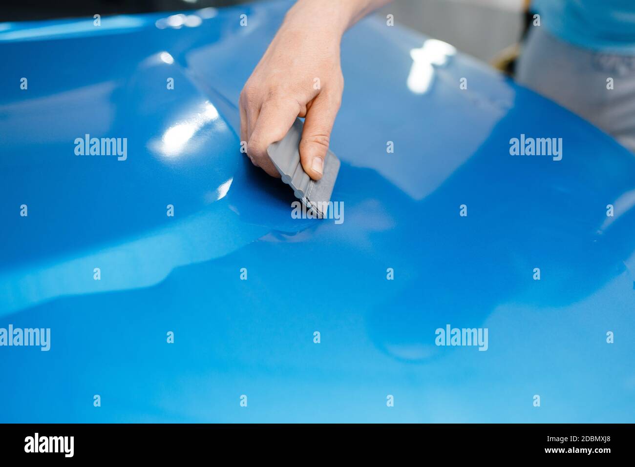 L'emballage de voiture, mécanique avec raclette, installe du film de protection en vinyle ou du film sur le capot du véhicule. L'employé effectue l'habillage automatique. Protection de peinture automobile Banque D'Images