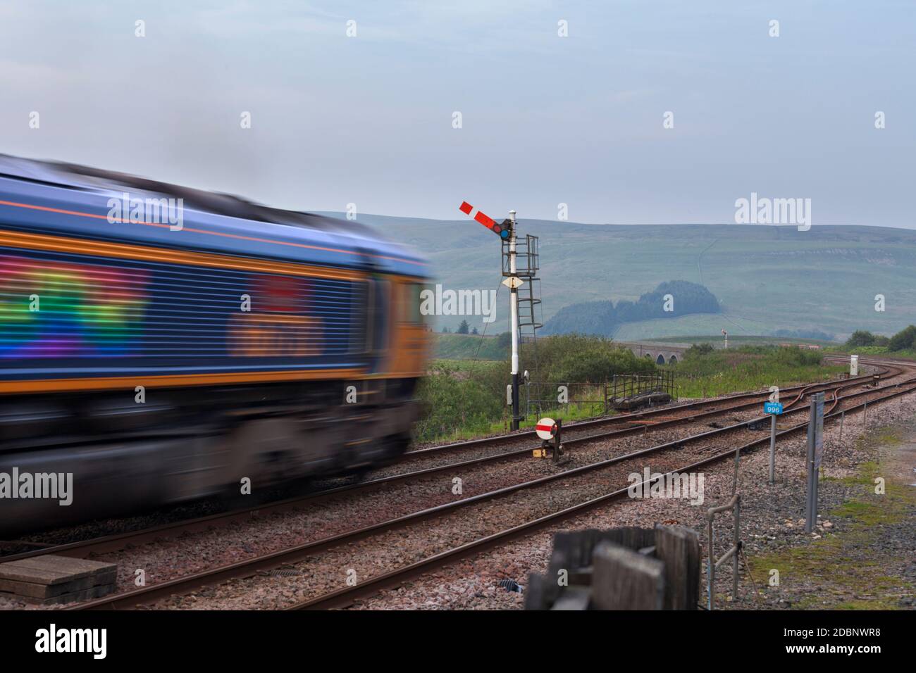 GB Railfreight classe 66 locomotive passant un signal de sémaphore de train du quadrant supérieur à Garsdale, Cumbria avec le flou de mouvement Banque D'Images