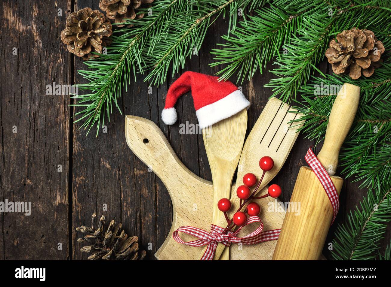Ustensiles de cuisine en bois avec chapeau de père Noël et cônes de pin sur fond de bois rustique foncé. Vue de dessus avec espace de copie pour votre texte. La cuisine de Noël Banque D'Images