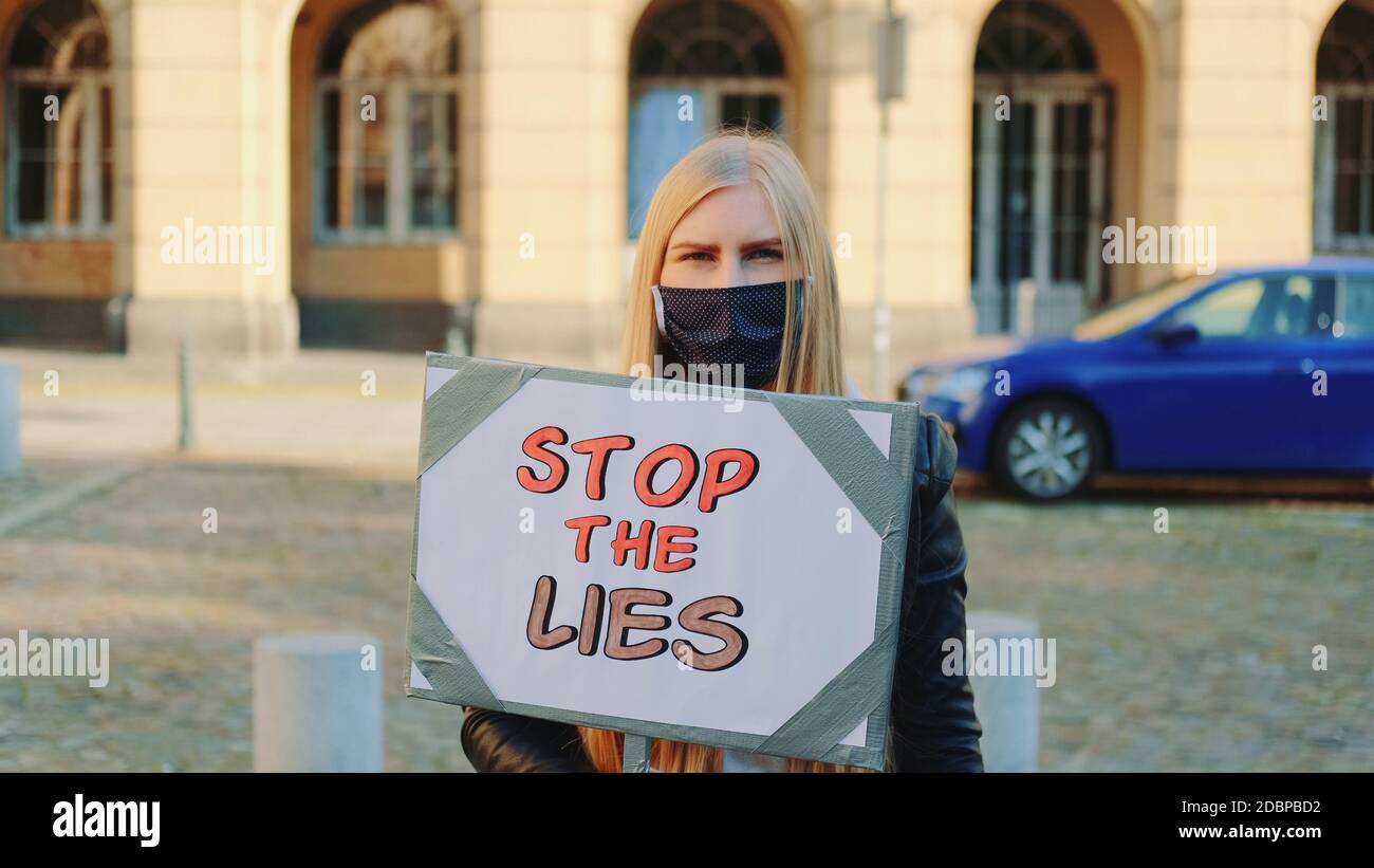 Femme inquiète dans un masque de protection avec une bannière de protestation appelant à arrêtez-vous en marchant dans la rue de la ville Banque D'Images
