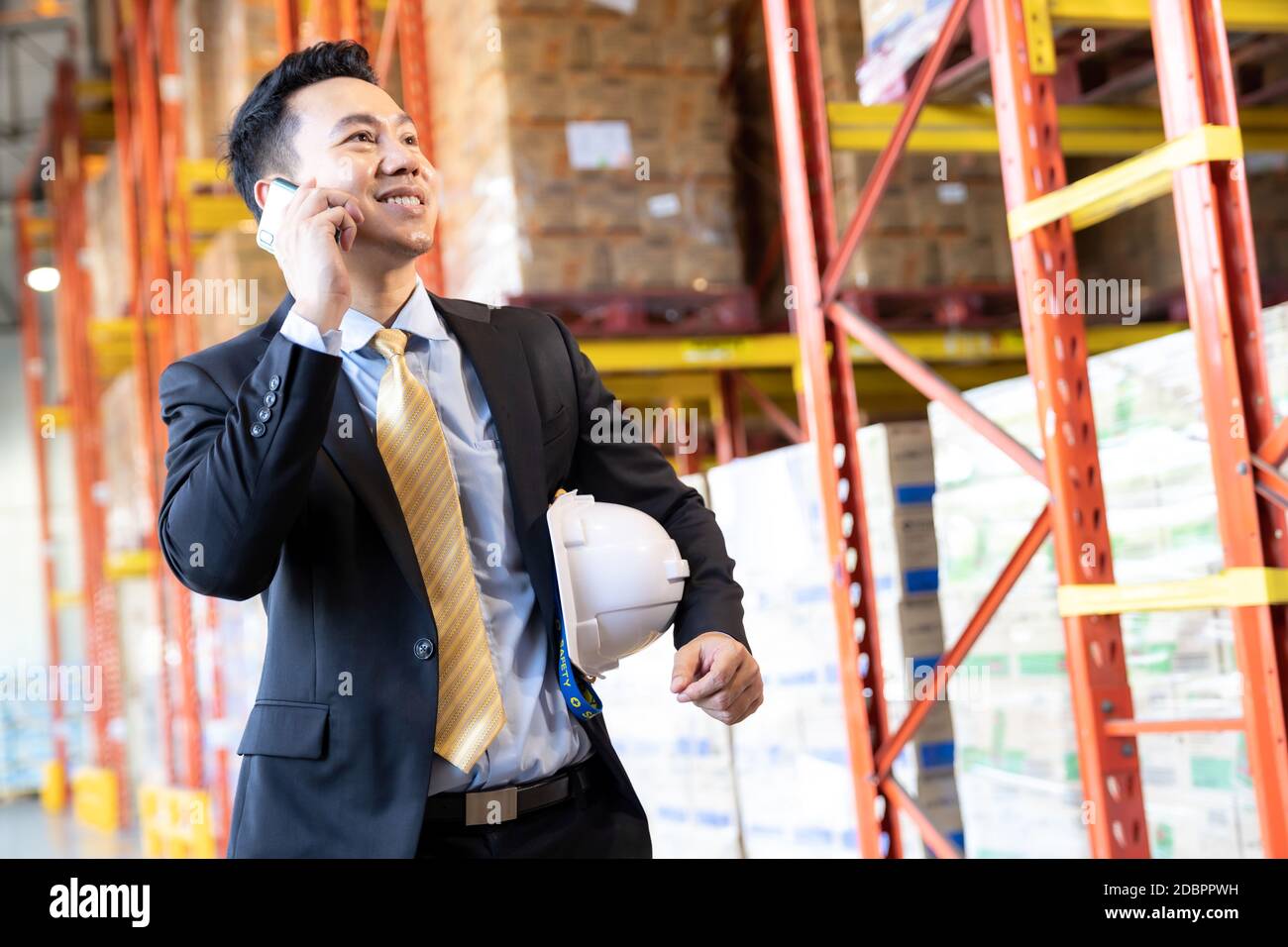 Portrait de confiance asiatique investisseur d'homme d'affaires stand et de faire un appel avec le téléphone mobile dans les grandes usines et l'environnement de distribution entrepôt. Banque D'Images