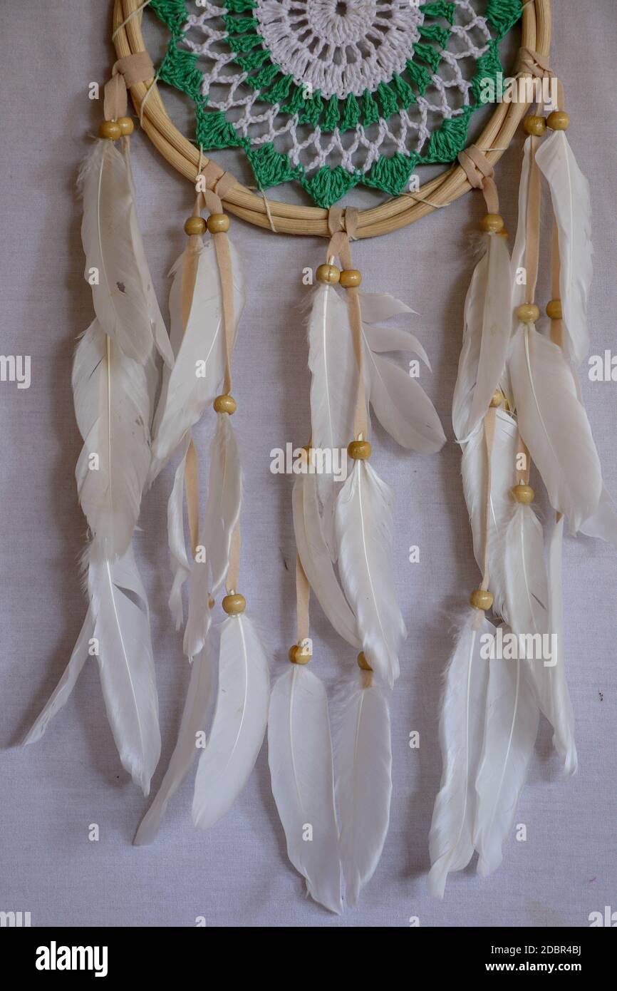 Attrape-rêve rose fait main avec du méli blanc sur fond de rochers et de lac. Éléments tribaux, plumes, dentelle, flocon de neige en crochet. Banque D'Images