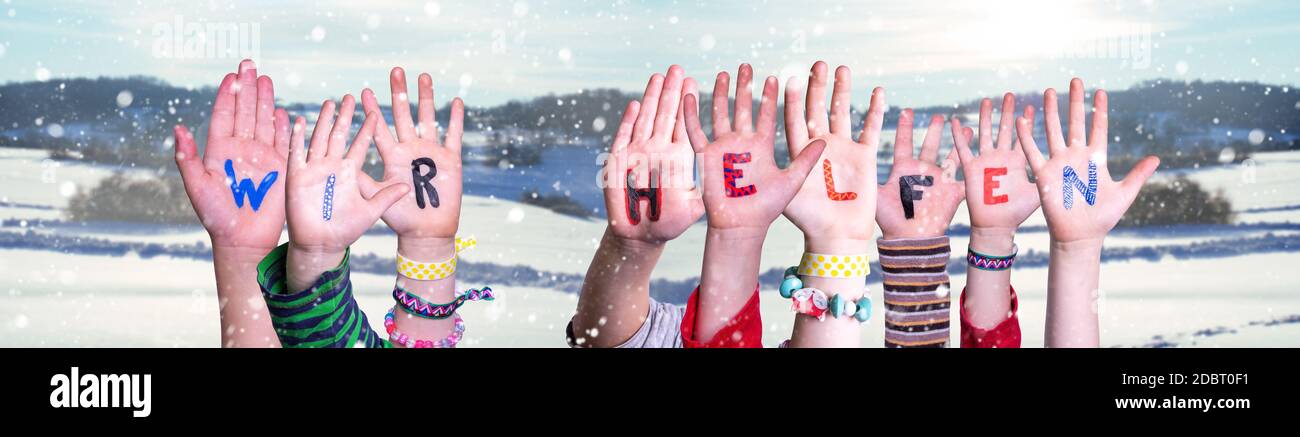 Les mains d'enfants tenant le mot allemand coloré Wir Helfen signifie que nous aide. Fond d'hiver enneigé avec flocons de neige Banque D'Images