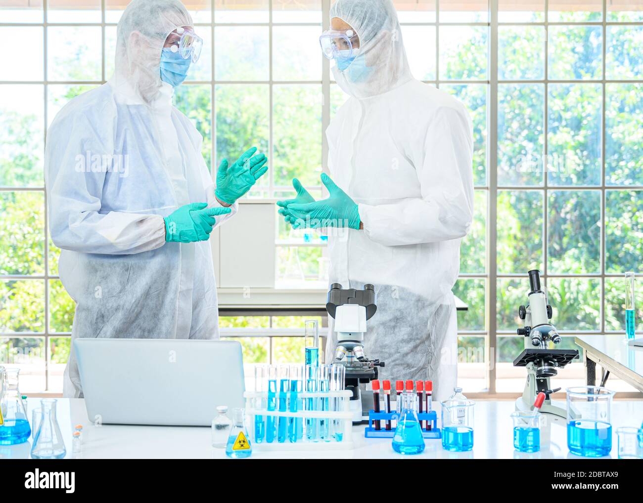 Couple de scientifiques mâles portant une combinaison de protection travaillant avec le microscope et de nombreux équipements de laboratoire pour la recherche de vaccins en laboratoire. Chercheur médical sp Banque D'Images