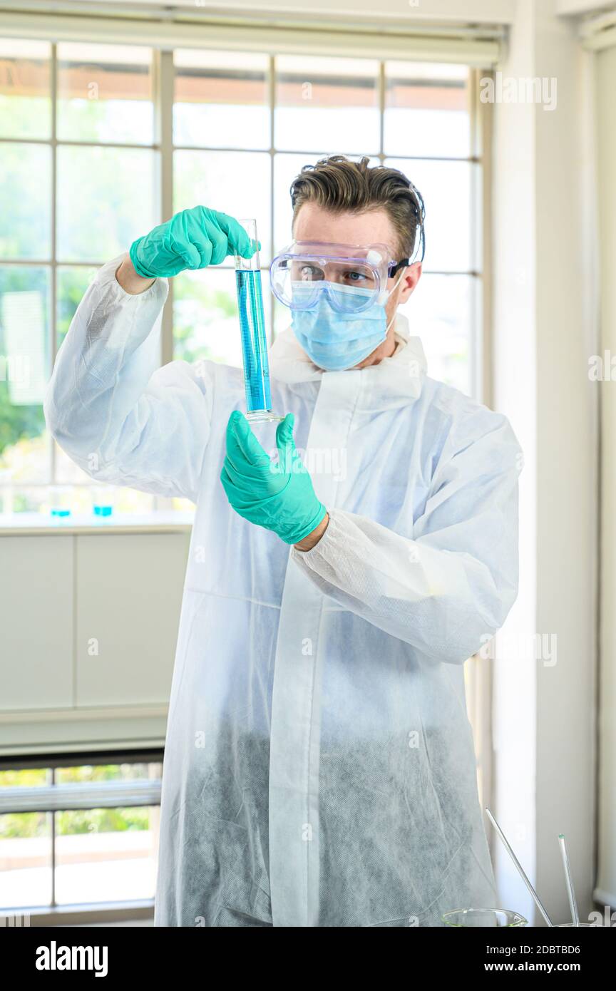 Un scientifique mâle porte une combinaison de protection pour le maintien d'un bécher ou d'un tube avec prélever du liquide à l'intérieur et travailler avec de nombreux équipements de laboratoire pour recherche en laboratoire Banque D'Images