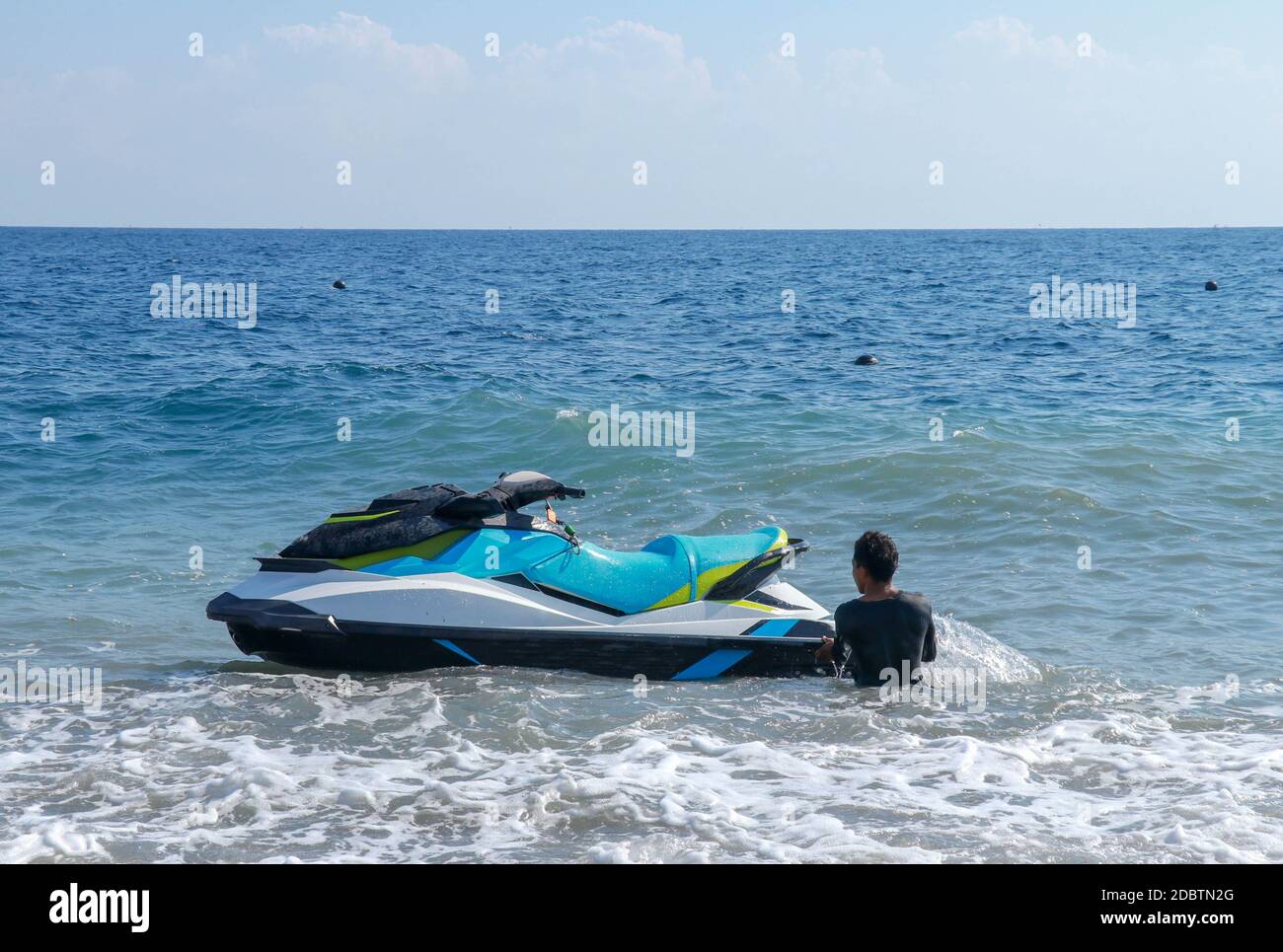 Jet ski flottant sur l'eau de mer bleue. Des bateaux puissants attendent les clients. Jeune indonésien tenant un jetbike près du rivage. Banque D'Images