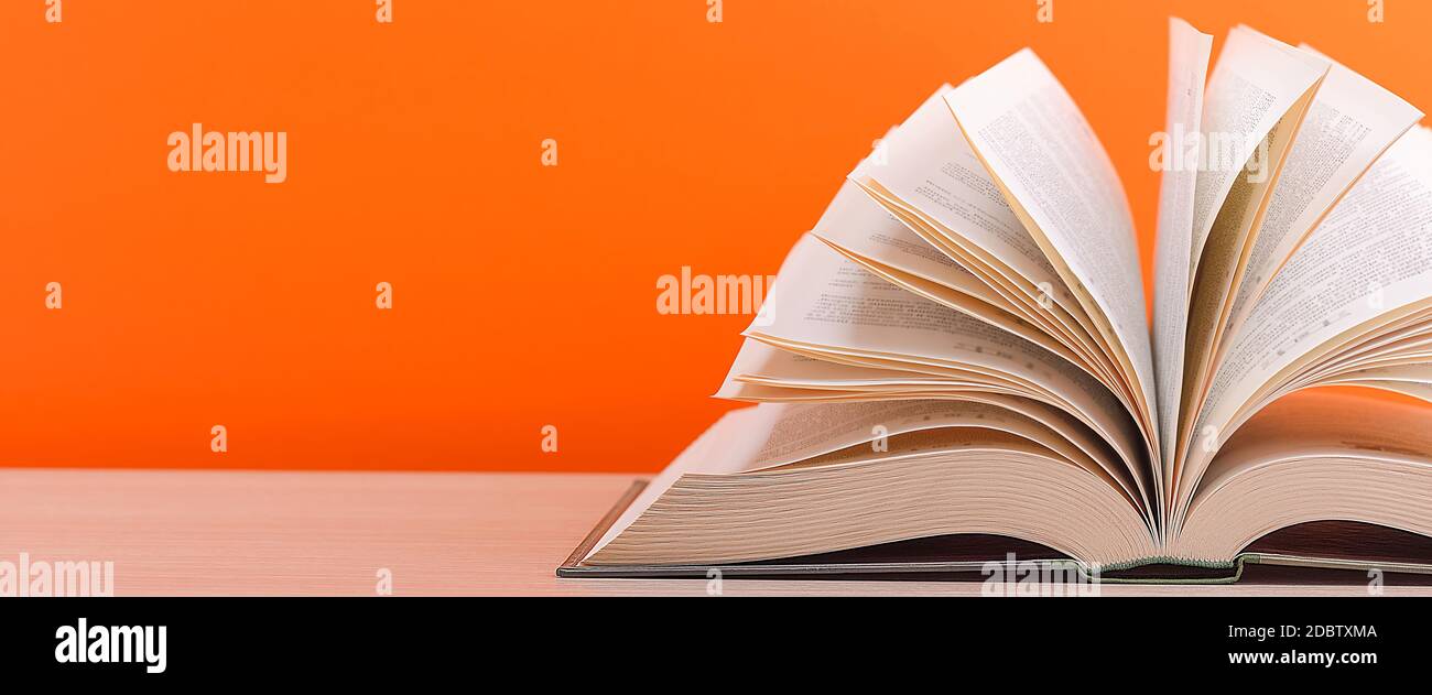 Un grand livre de couverture rigide épais repose sur une table en bois clair. Le livre est ouvert, les feuilles de la page sont défonsées, et le verso est un fond orange Banque D'Images