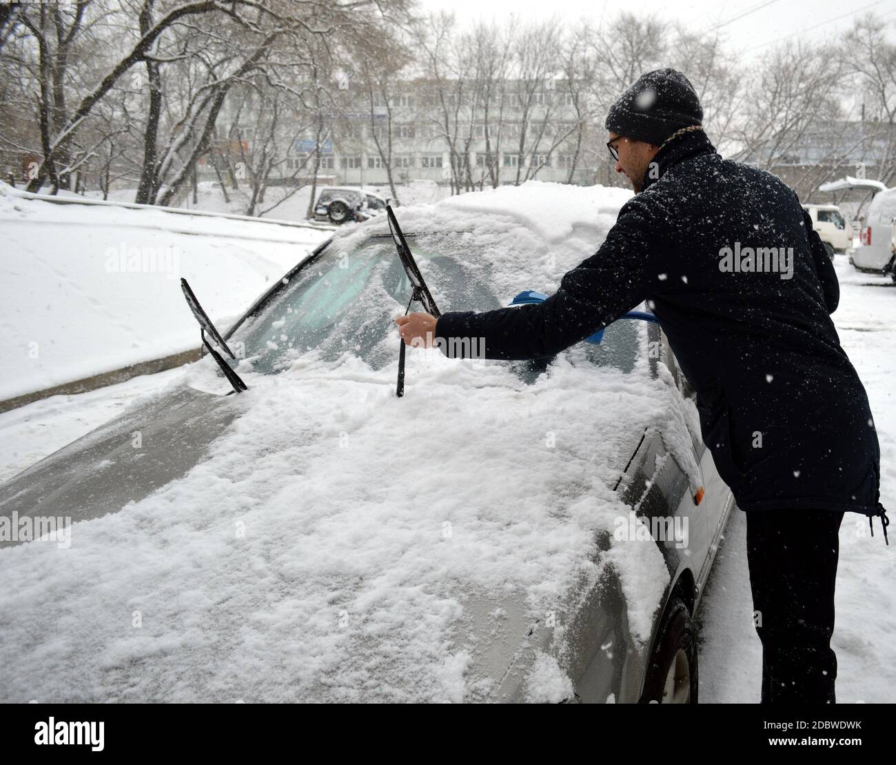 Un jeune homme balaie la neige de la voiture et des balais d'essuie-glace par une journée de neige froide en hiver Banque D'Images Un jeune homme balaie la neige de la voiture et des balais d'essuie-glace par une journée de neige froide en hiver Banque D'Images
