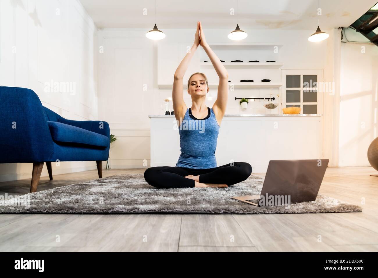 Blanc caucasien tenue sportive femme faisant le yoga Sukhasana s'asseoir poser dans le salon à la maison regardant les tutoriels en ligne de l'entraîneur sur ordinateur portable. L'activité, f Banque D'Images