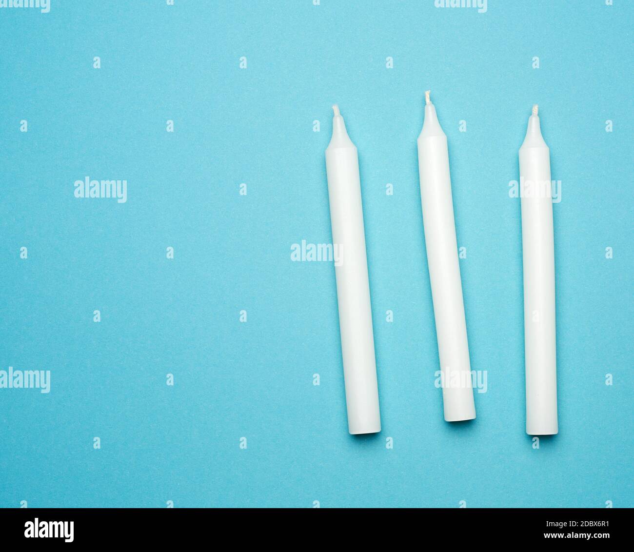 trois bougies de cire blanche sur fond bleu, plat, espace de copie Banque D'Images
