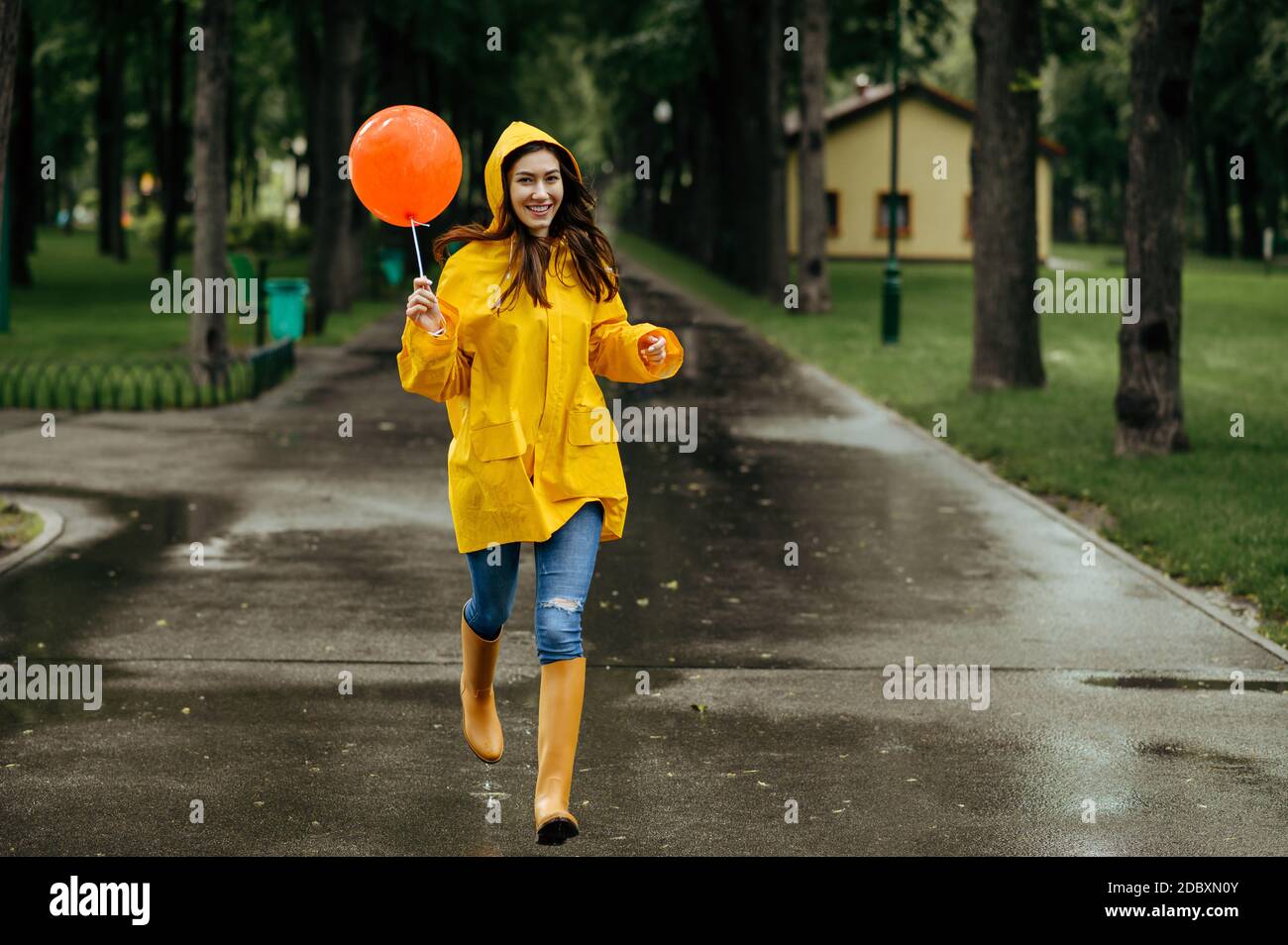 Une femme heureuse court avec un ballon dans le parc d'été par temps  pluvieux. Femme en cape de pluie et bottes en caoutchouc, temps humide dans  une allée, solitude Photo Stock -