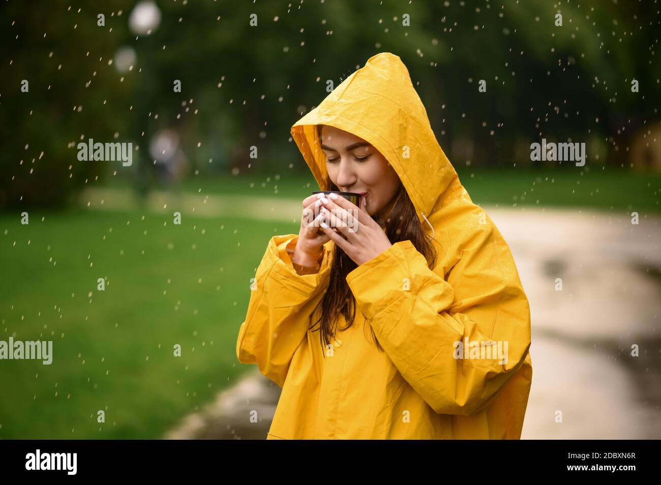 Une femme en imperméable boit du thé chaud dans le parc d'été, le jour des  pluies. Seule femme en cape pluie sur un sentier de randonnée, temps humide  dans une allée Photo