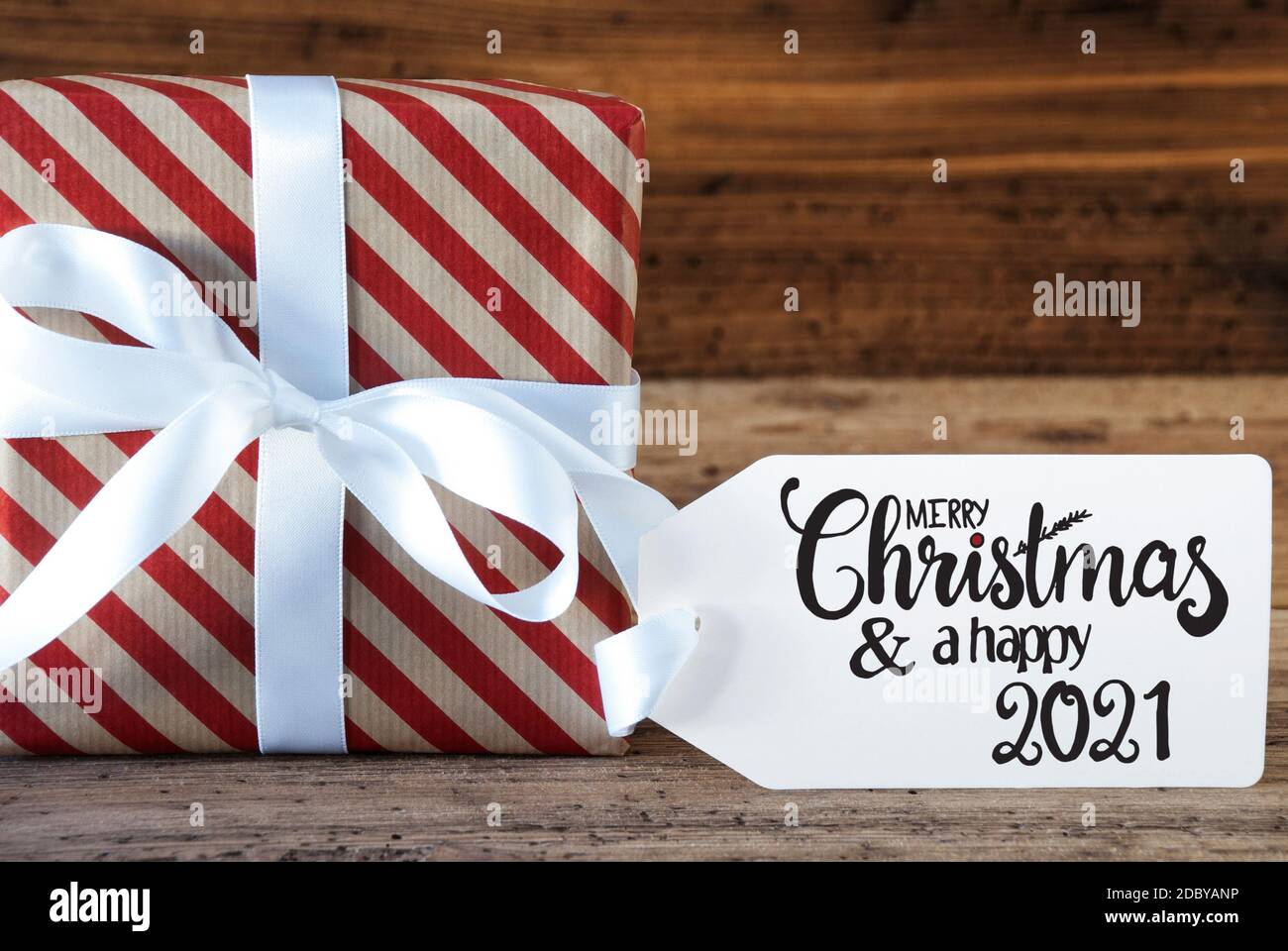 Un cadeau de Noël avec étiquette avec la calligraphie anglaise Joyeux Noël et UN heureux 2021. Papier d'emballage avec un noeud Banque D'Images